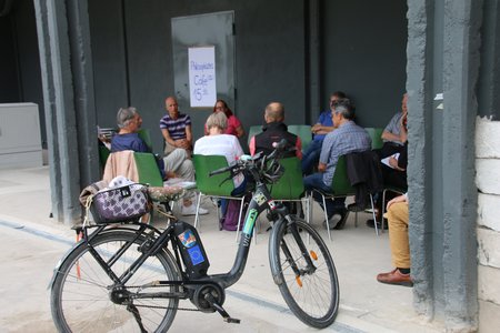 Menschen sitzen draußen in einem Stuhlkreis, im Vordergrund ein Fahrrad