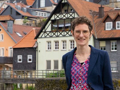 Hinter Prof. Dr. Sophia Frank sind pittoreske Fachwerkhäuser des Standortes Kronach der Hochschule Coburg zu sehen.