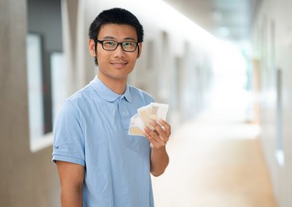 Ein Mann hält in der Hochschule Coburg einige Plastikhüllen mit Mustern in der Hand.