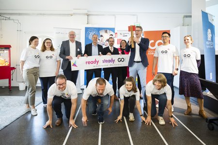 Das Team des Gründungshub Oberfranken Go! auf einer Laufbahn. issenschaftsminister Markus Blume mit einer Starterklappe.