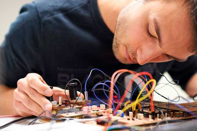 A person from Hochschule Coburg is fully engrossed in assembling an electronic circuit board, skillfully navigating through a tangle of colorful wires and components.