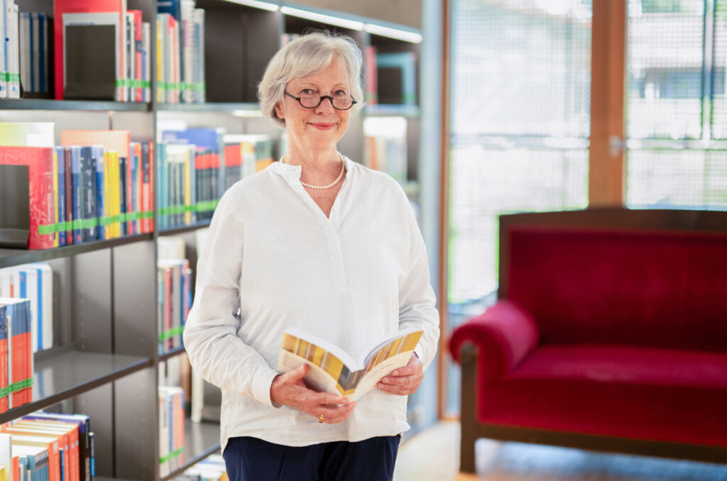 Prof. Dr. Veronika Hammer, Professorin der Fakultät Soziale Arbeit der Hochschule Coburg, steht vor einem Bücherregal und hält ein Buch in Händen.