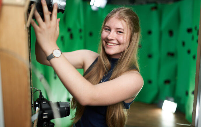 Eine junge Frau steht in einem 3D-Rig und lächelt in die Kamera.