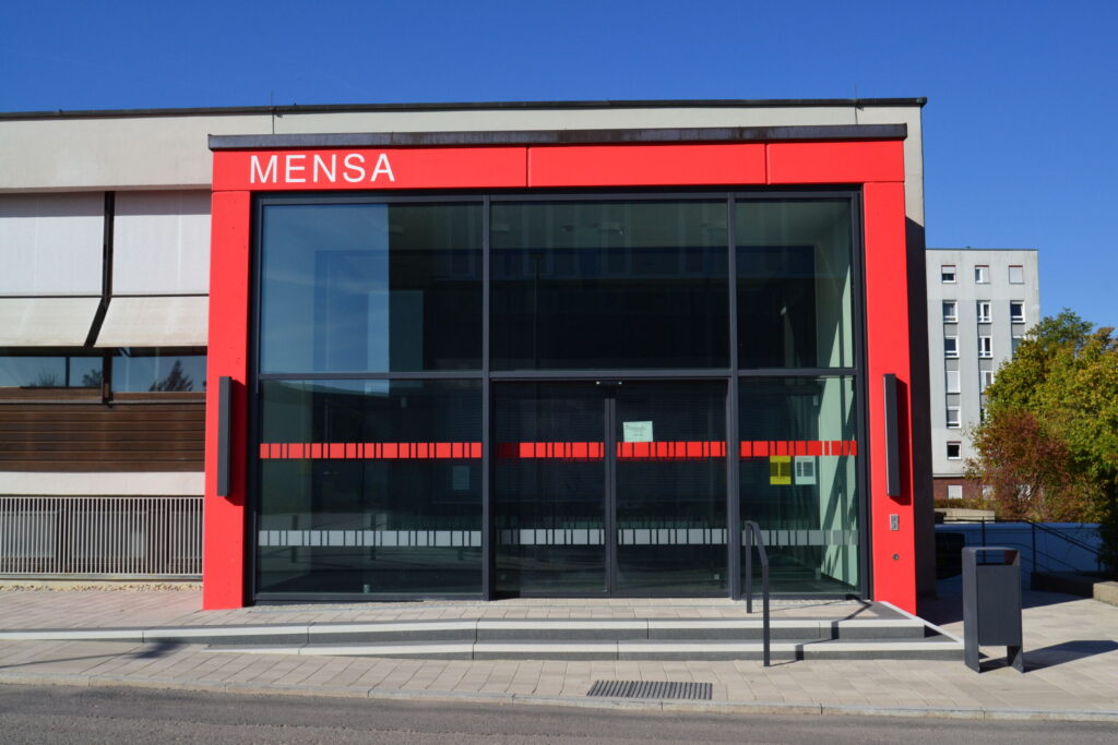 Modern building with a red-framed glass entrance labeled "MENSA" at the top. The structure, part of Hochschule Coburg