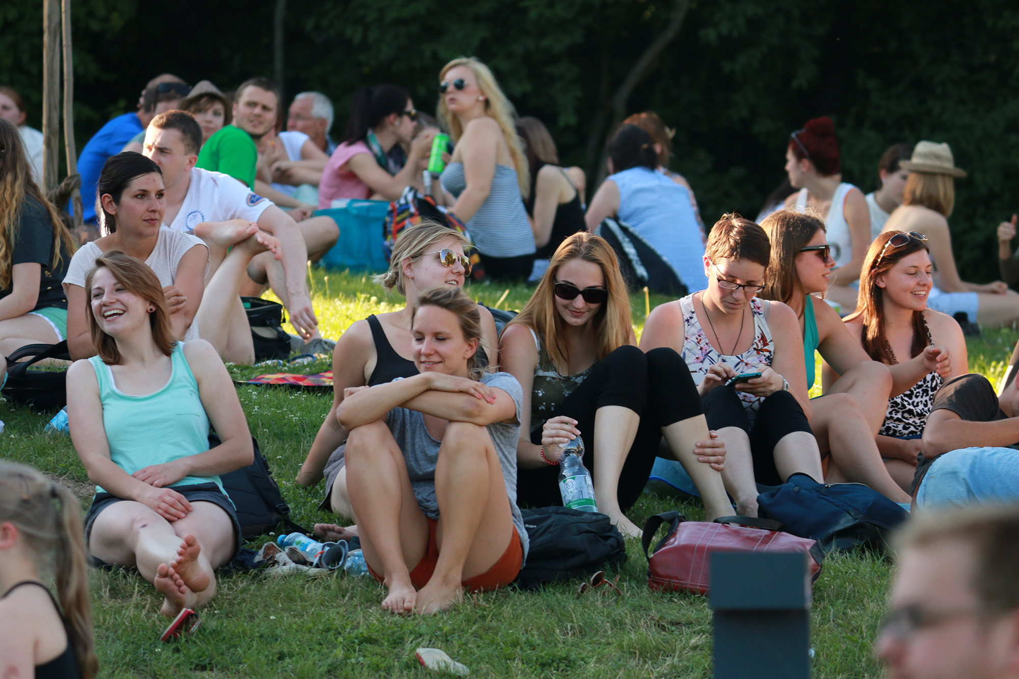 Eine Gruppe von Menschen sitzt auf der Wiese in einem Park in der Nähe der Hochschule Coburg, lacht und genießt einen sonnigen Tag. Einige unterhalten sich, andere entspannen sich selig. Bäume spenden Schatten und verstärken die ruhige Atmosphäre.