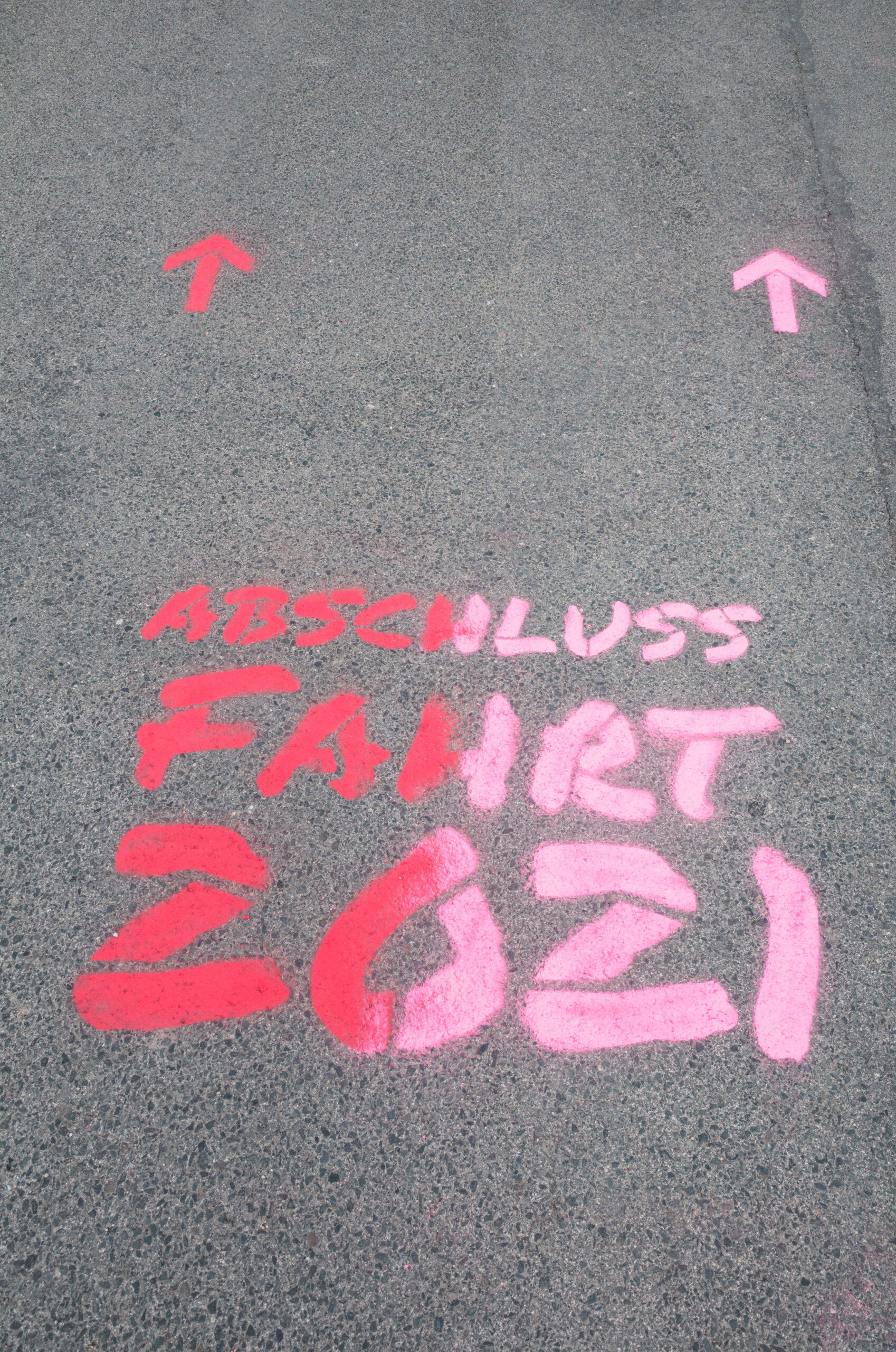 Auf dem Bürgersteig befindet sich ein rosa-rotes Graffiti mit der Aufschrift „Abschluss Fahrt 2021“ und zwei nach vorne zeigenden rosa Pfeilen, das den lebendigen Geist der Hochschule Coburg einfängt.