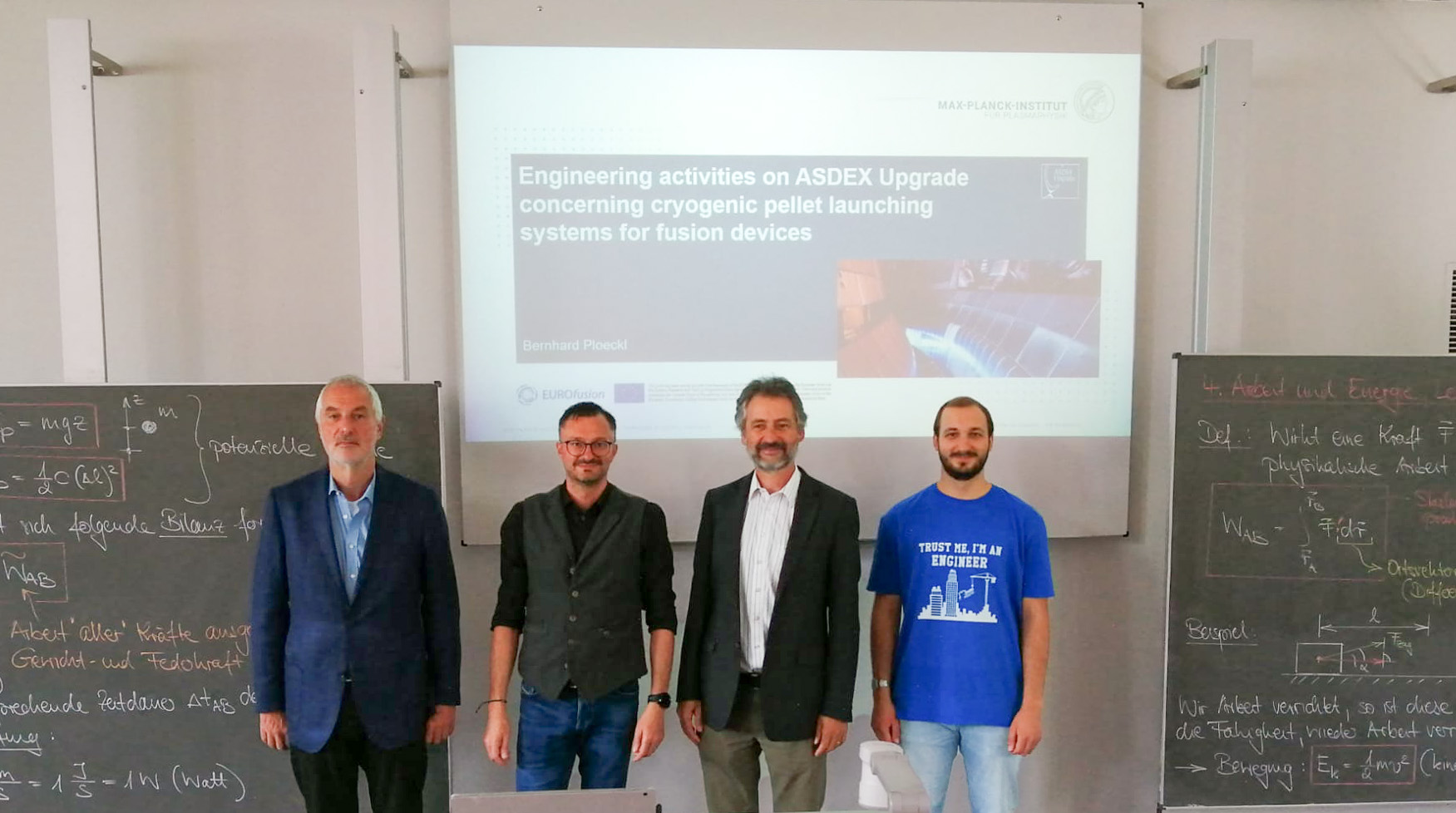 Vier Personen stehen vor einer Präsentationsfolie mit dem Titel „Ingenieuraktivitäten an ASDEX Upgrade zu Startsystemen für kryogene Pellets für Fusionsanlagen“ an der Hochschule Coburg. Neben ihnen stehen zwei Tafeln mit Gleichungen, die ihre wissenschaftliche Arbeit hervorheben.