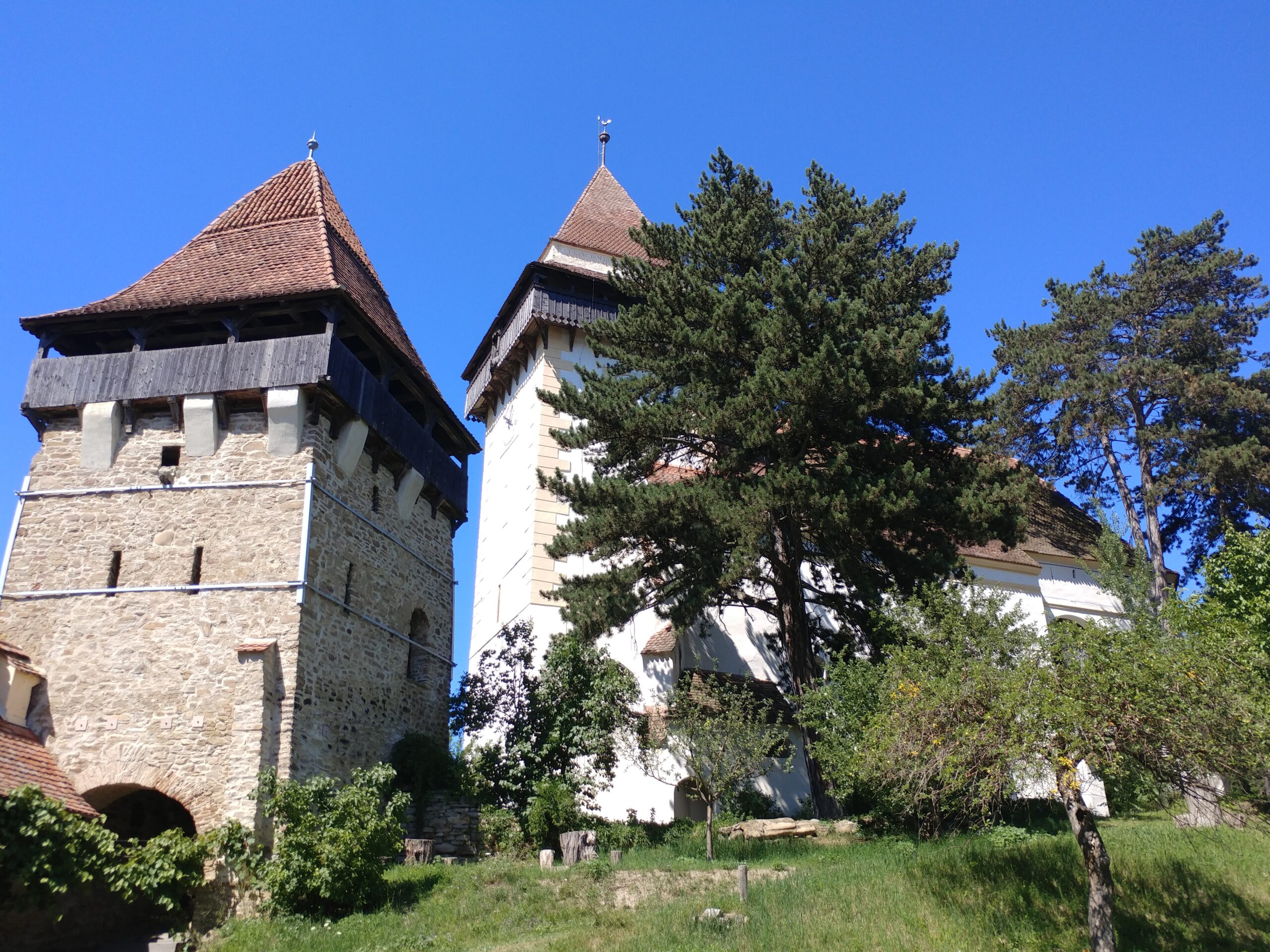 Diese historische Wehrkirche in der Nähe der Hochschule Coburg verfügt über zwei Türme und Steinmauern, umgeben von üppigem Grün und Gras unter einem klaren blauen Himmel.