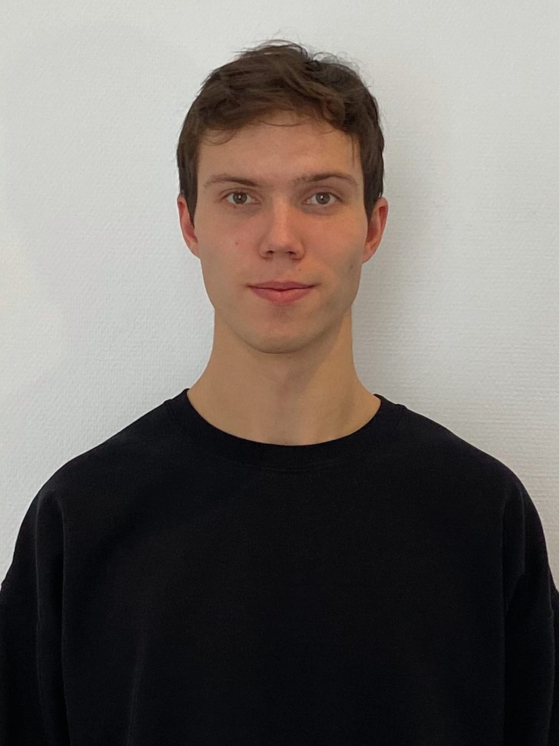 A person with short brown hair, wearing a black sweater, stands against a plain white background, embodying the essence of Hochschule Coburg's modern style while looking directly at the camera.