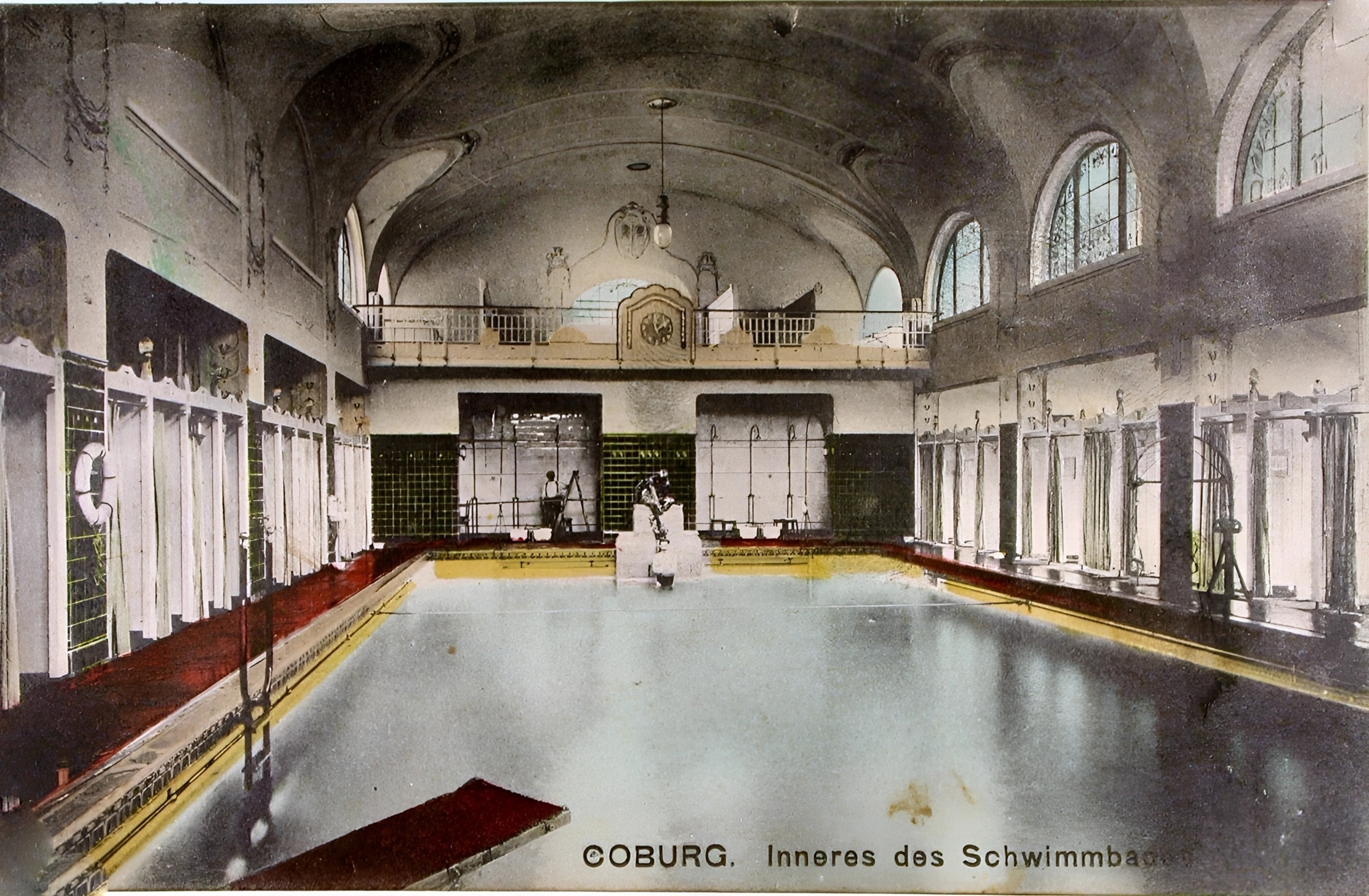 A vintage photograph captures the indoor swimming pool in Coburg, surrounded by arched windows and decorated tiles. Labeled "Coburg. Inneres des Schwimmbades," it hints at the historic charm of Hochschule Coburg's architecture within a classic bathhouse setting.