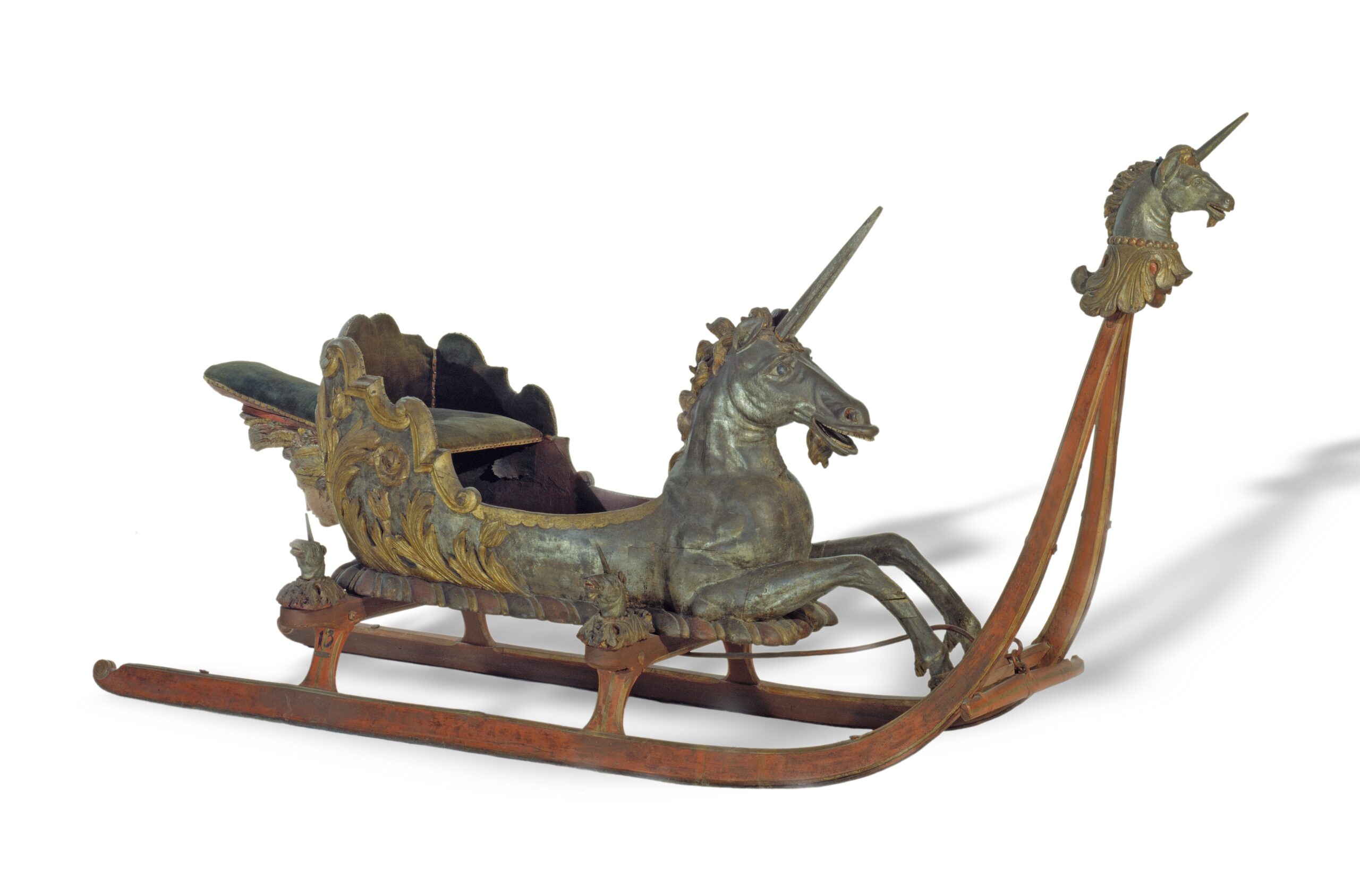 This ornate antique sleigh, reminiscent of the craftsmanship taught at Hochschule Coburg, boasts detailed carvings of unicorns on the front. It features intricate designs and wooden runners, showcasing a perfect blend of artistry and skilled craftsmanship.