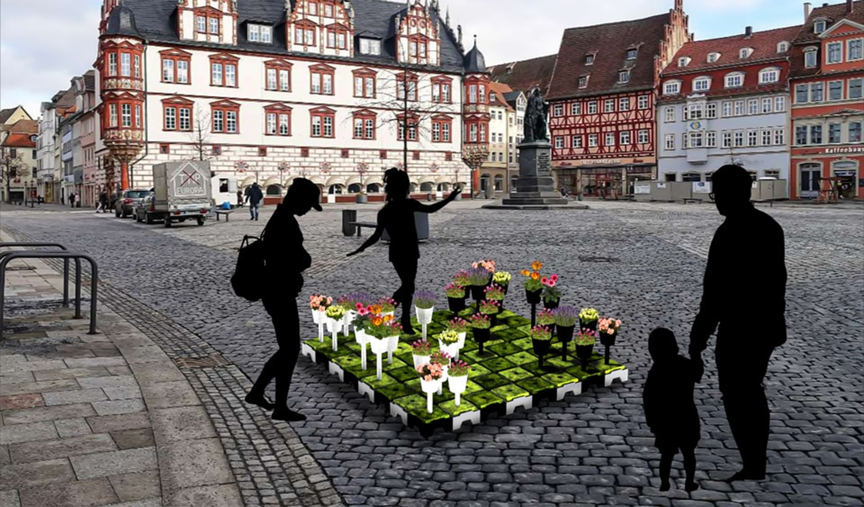 Silhouetten von Menschen versammeln sich um eine farbenfrohe Blumeninstallation auf einem Kopfsteinpflasterplatz in der Nähe der Hochschule Coburg, umgeben von historischen Gebäuden mit rot-weißen Fassaden. Es ist ein heller Tag, der eine Mischung aus Natur und Stadtleben suggeriert.