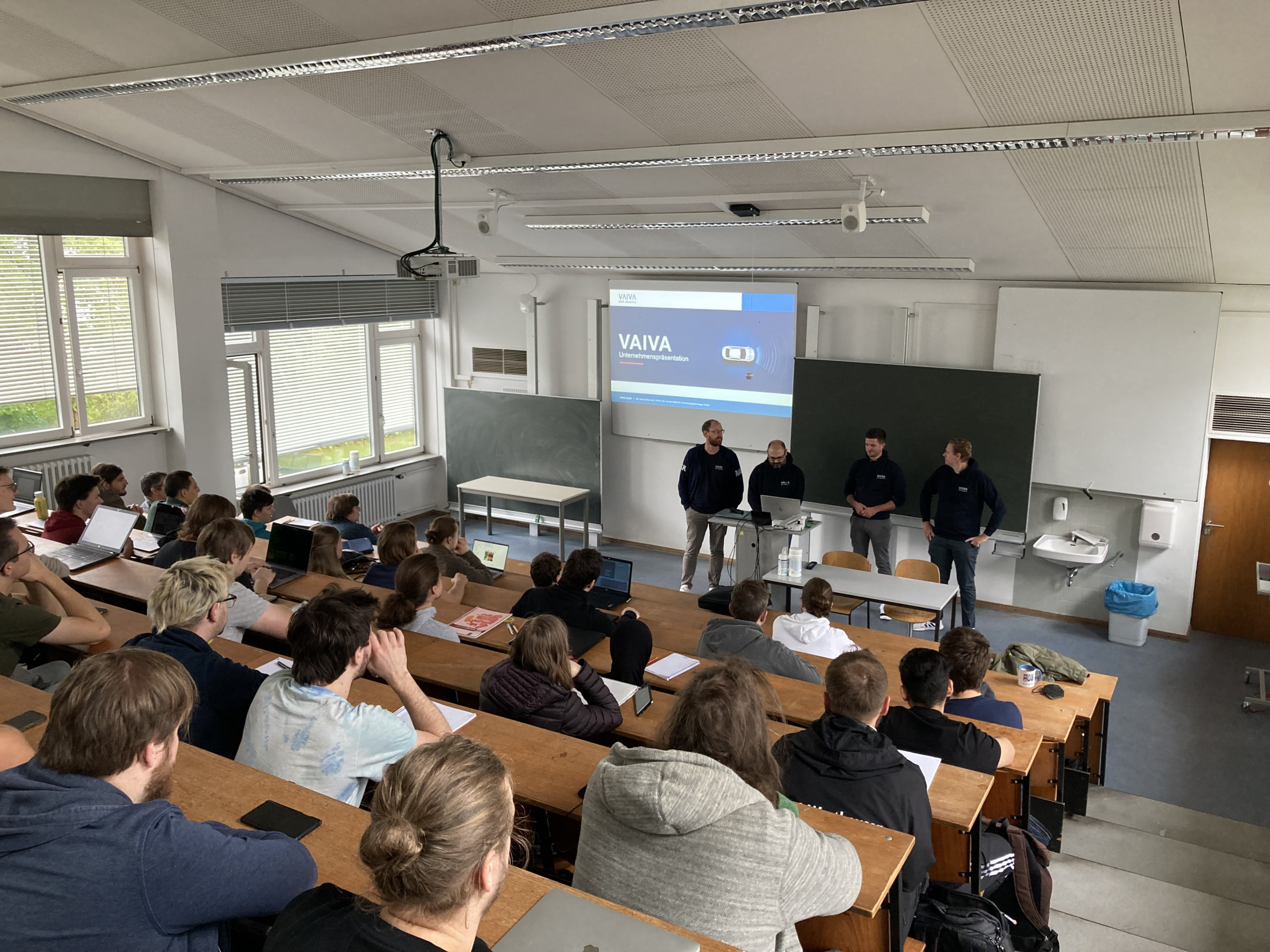 In einem Hörsaal der Hochschule Coburg herrscht reges Treiben. An Holztischen sitzen Studenten, denen vier Vortragende gegenüberstehen. Auf der Leinwand hinter ihnen wird „VAIVA“ projiziert, begleitet vom Sonnenlicht, das durch große Fenster fällt, und der klassischen Präsenz einer Tafel.