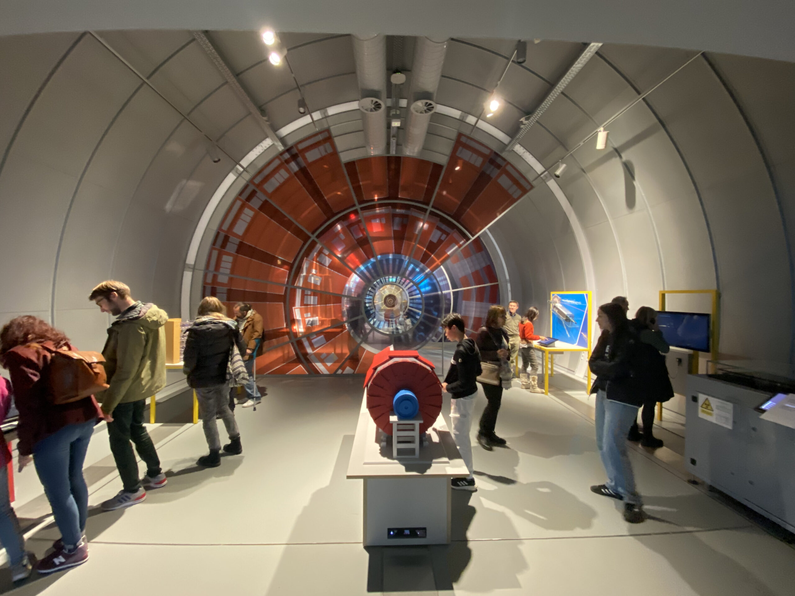 In einem großen, runden Tunnel mit farbenfrohem, futuristischem Design können Besucher an der Hochschule Coburg eine interaktive Wissenschaftsausstellung erkunden. Zahlreiche Displays und Bildschirme säumen die Wände und regen die Besucher zu einer Vielzahl spannender Aktivitäten an.