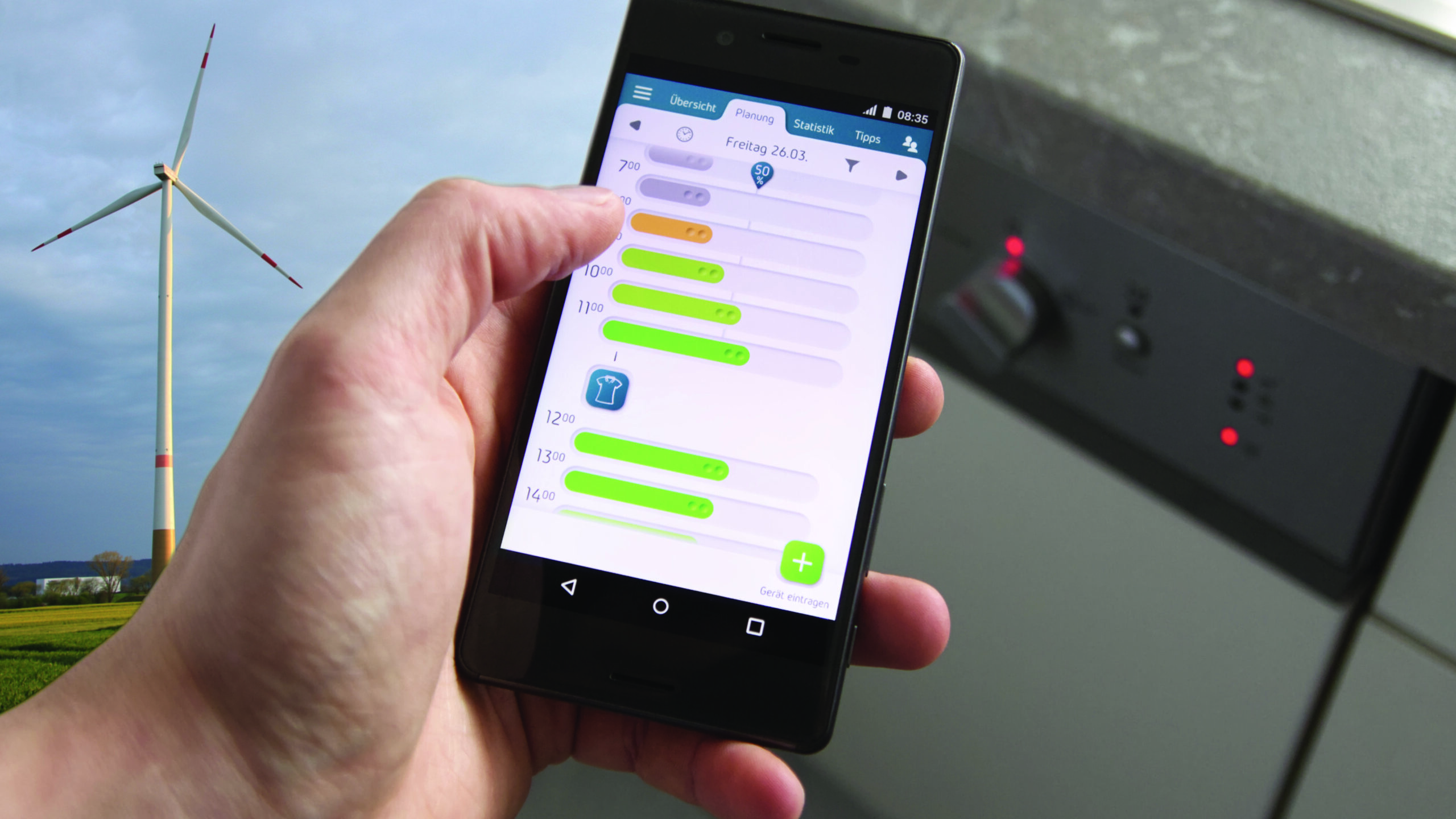 Eine Person hält ein Smartphone, auf dem eine Energiemanagement-App der Hochschule Coburg mit bunten Verbrauchsbalken angezeigt wird. Im Hintergrund steht eine Windturbine, die die Integration erneuerbarer Energien symbolisiert.