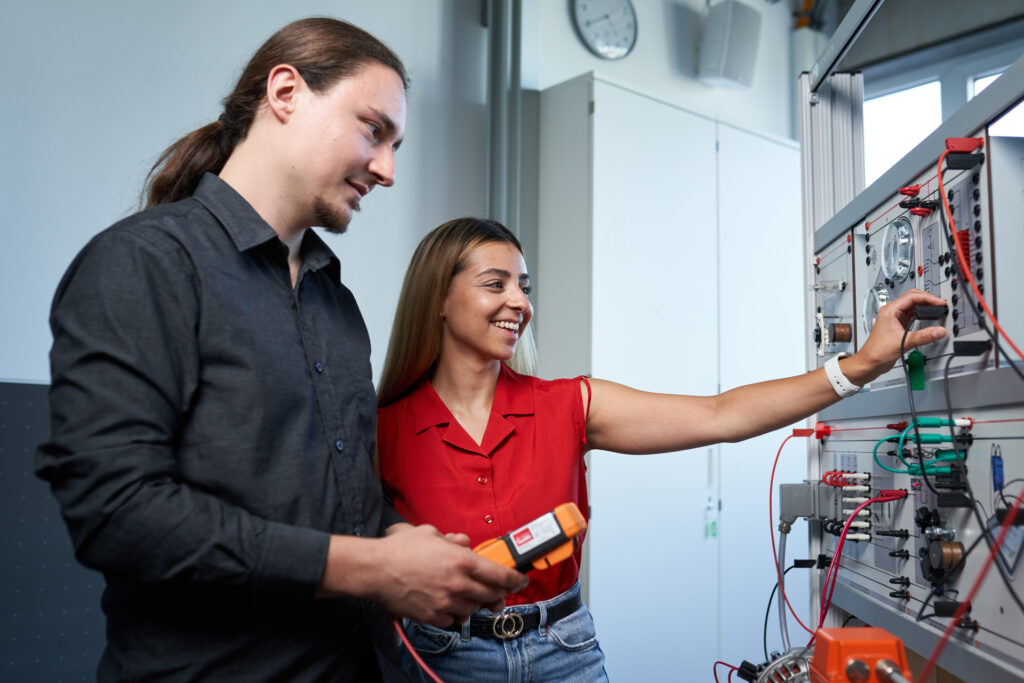 Studierende an einem Schaltkasten prüfen die Kabel