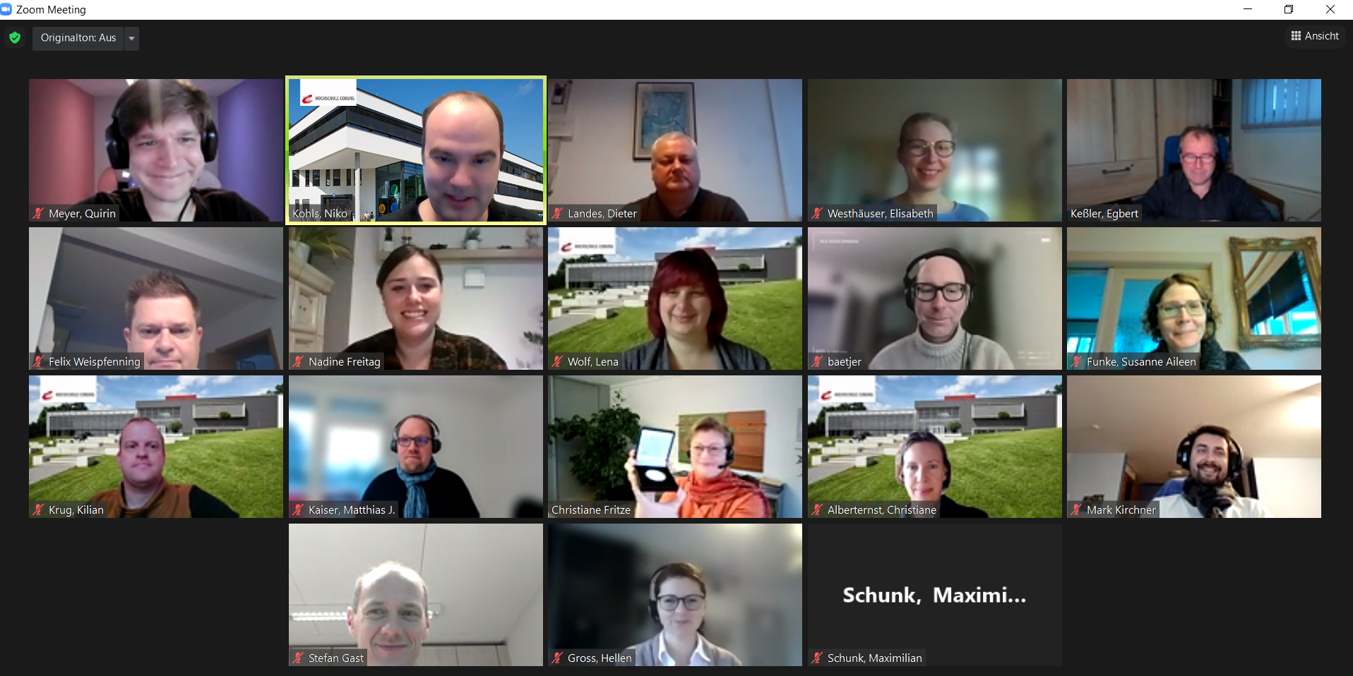 Screenshot eines virtuellen Zoom-Meetings mit 18 Teilnehmern, jeder in seinem eigenen Videoquadrat. Einige Hintergründe zeigen Bürogebäude und Außenszenen, die an die Hochschule Coburg erinnern. Unter jedem Teilnehmer werden Namen angezeigt, vor dem Hintergrund der vertrauten Zoom-Oberfläche.