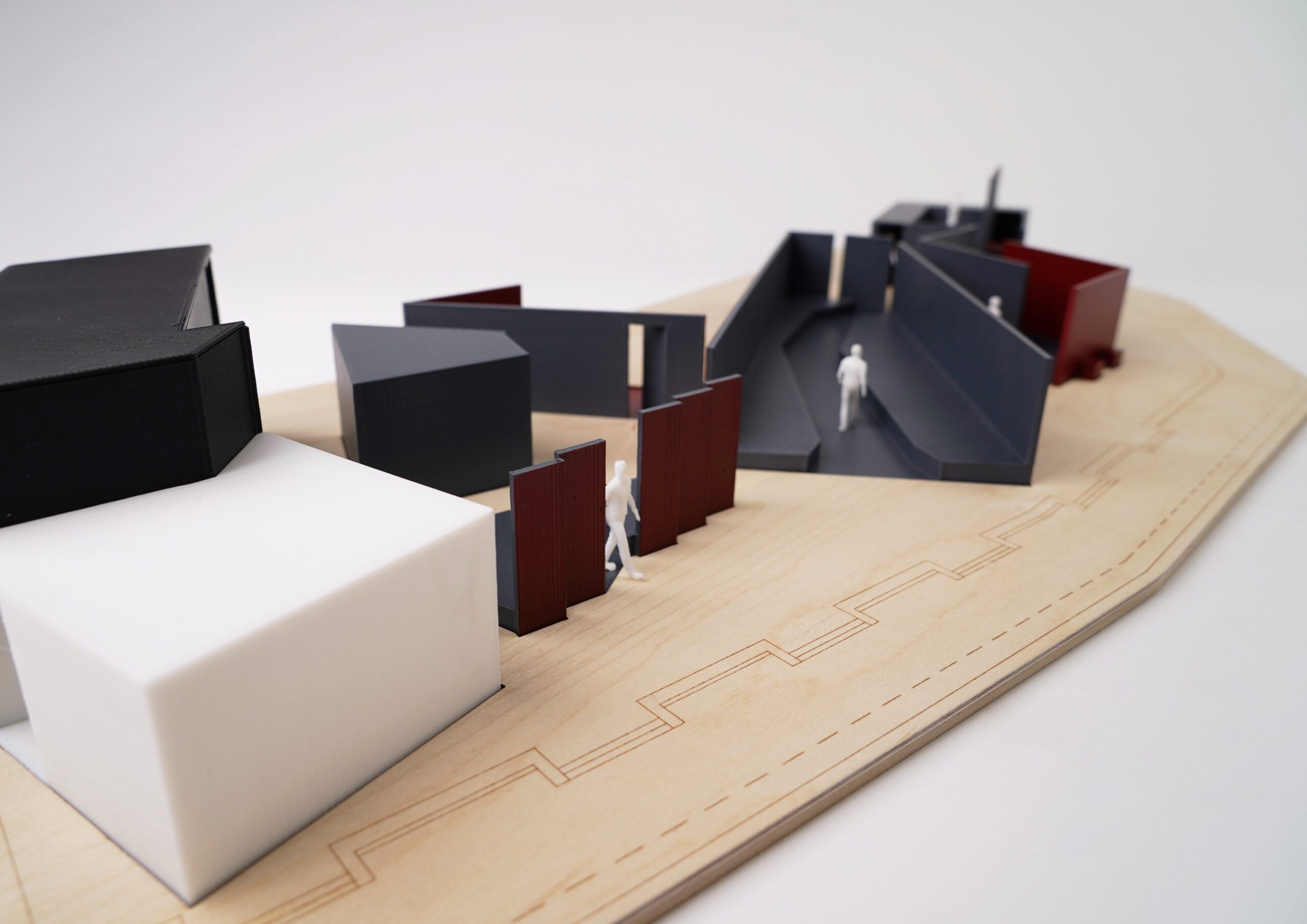 A minimalist architectural model on a wooden base, inspired by Hochschule Coburg's innovative design ethos, features geometric shapes in black, white, and red. Small white figurines are placed around the model, suggesting pathways and entrances.