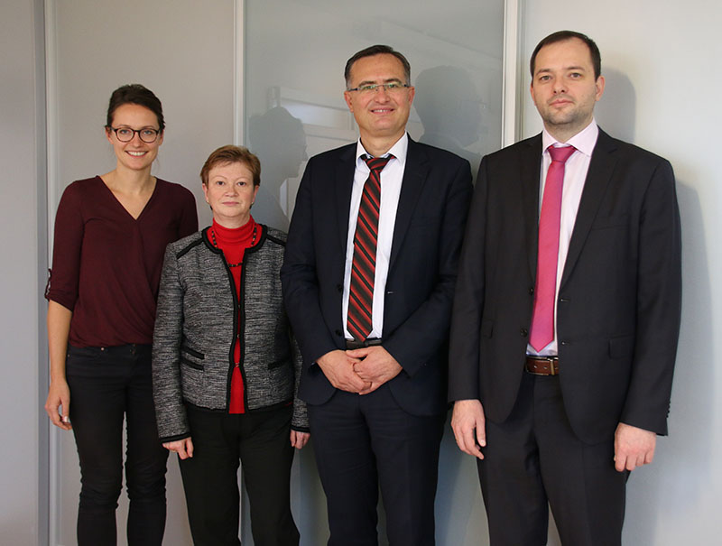 Vier Personen stehen nebeneinander, in Business-Kleidung gekleidet, vor einem neutralen Hintergrund an der Hochschule Coburg. Die beiden Frauen sind links und die beiden Männer rechts, alle mit neutralem Gesichtsausdruck.