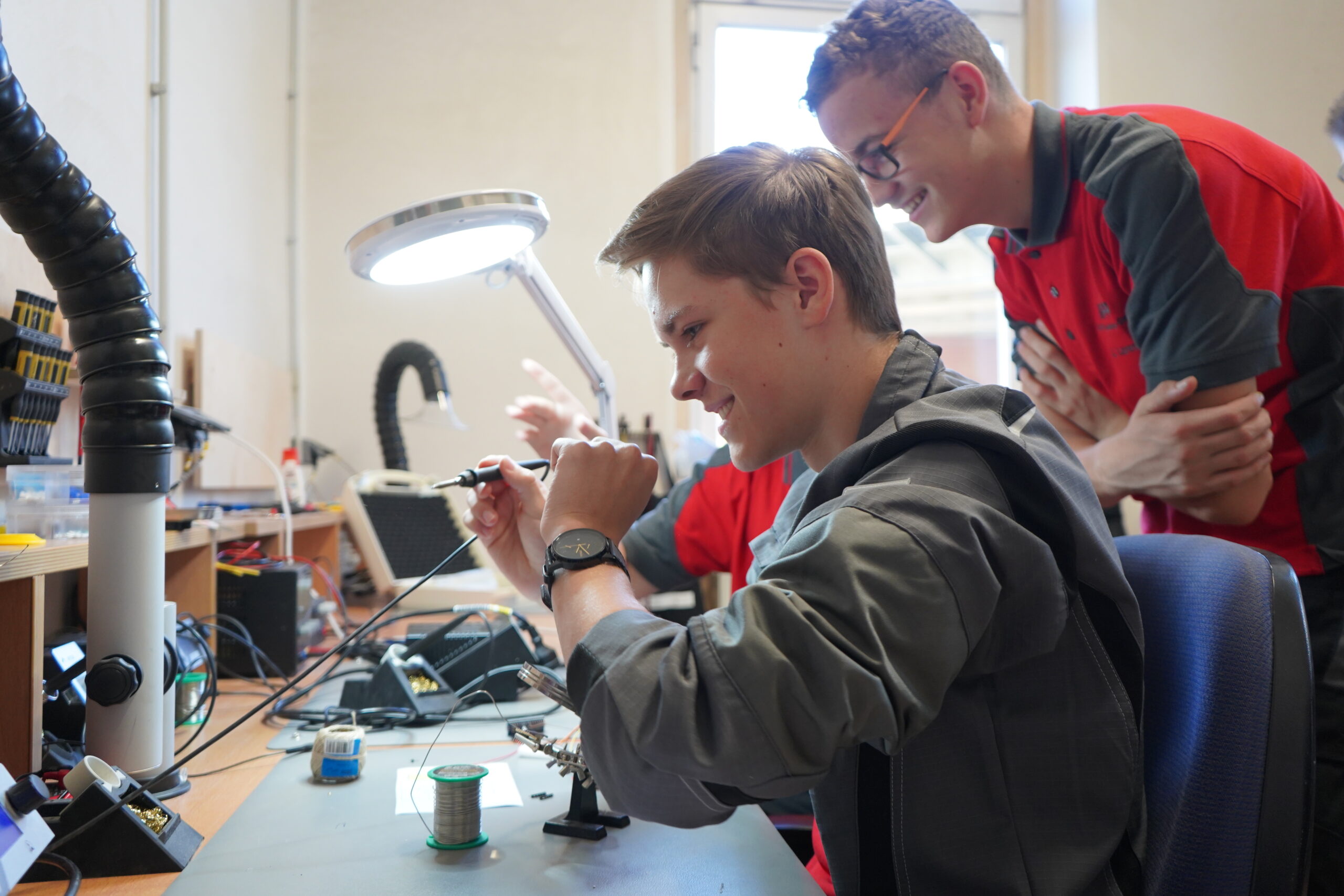 In einem geschäftigen Labor der Hochschule Coburg tauchen zwei junge Enthusiasten in die Elektronik ein. Einer lötet fachmännisch eine Platine, während der andere lächelnd zusieht. Umgeben von einer Vielzahl von Werkzeugen und Geräten liegt ihre Leidenschaft für Innovationen in der Luft.