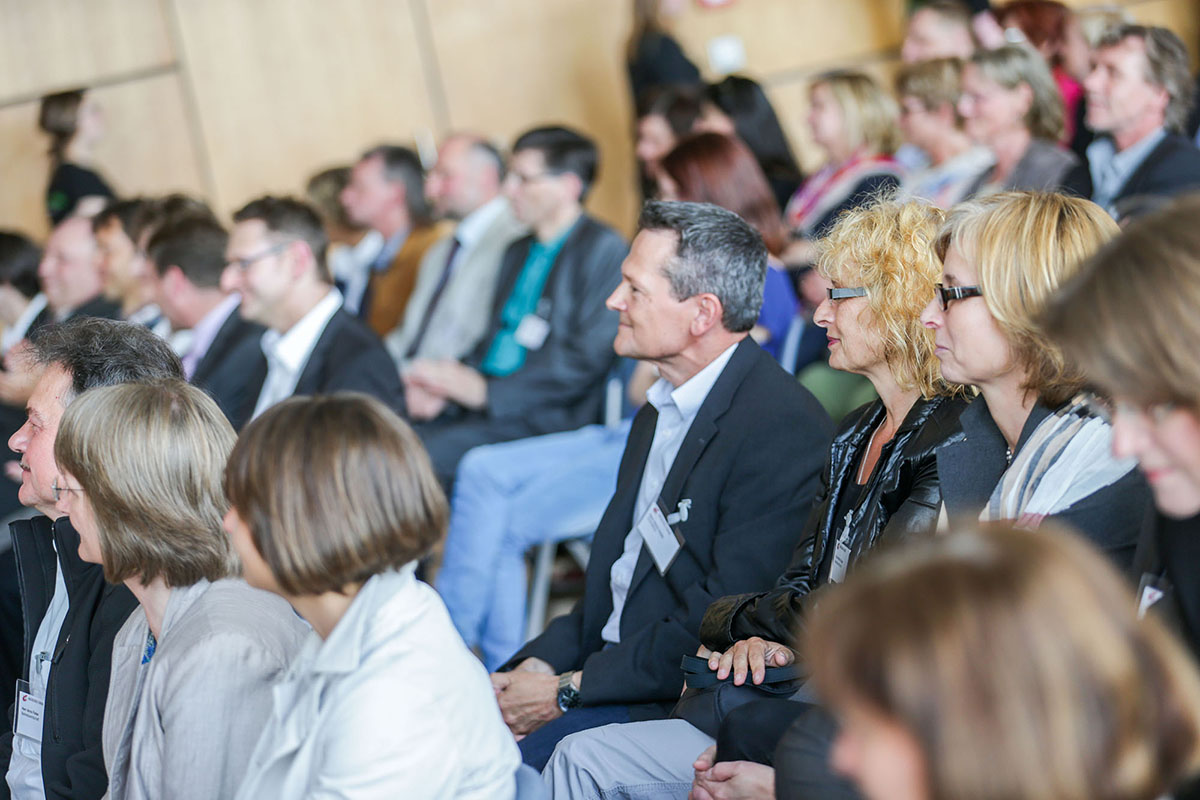 Eine Gruppe sitzender Menschen lauscht aufmerksam einem Vortrag an der Hochschule Coburg. Viele Sport-Namensschilder und Business-Kleidung vor einer hellen Wand sorgen für eine professionelle und konzentrierte Atmosphäre.