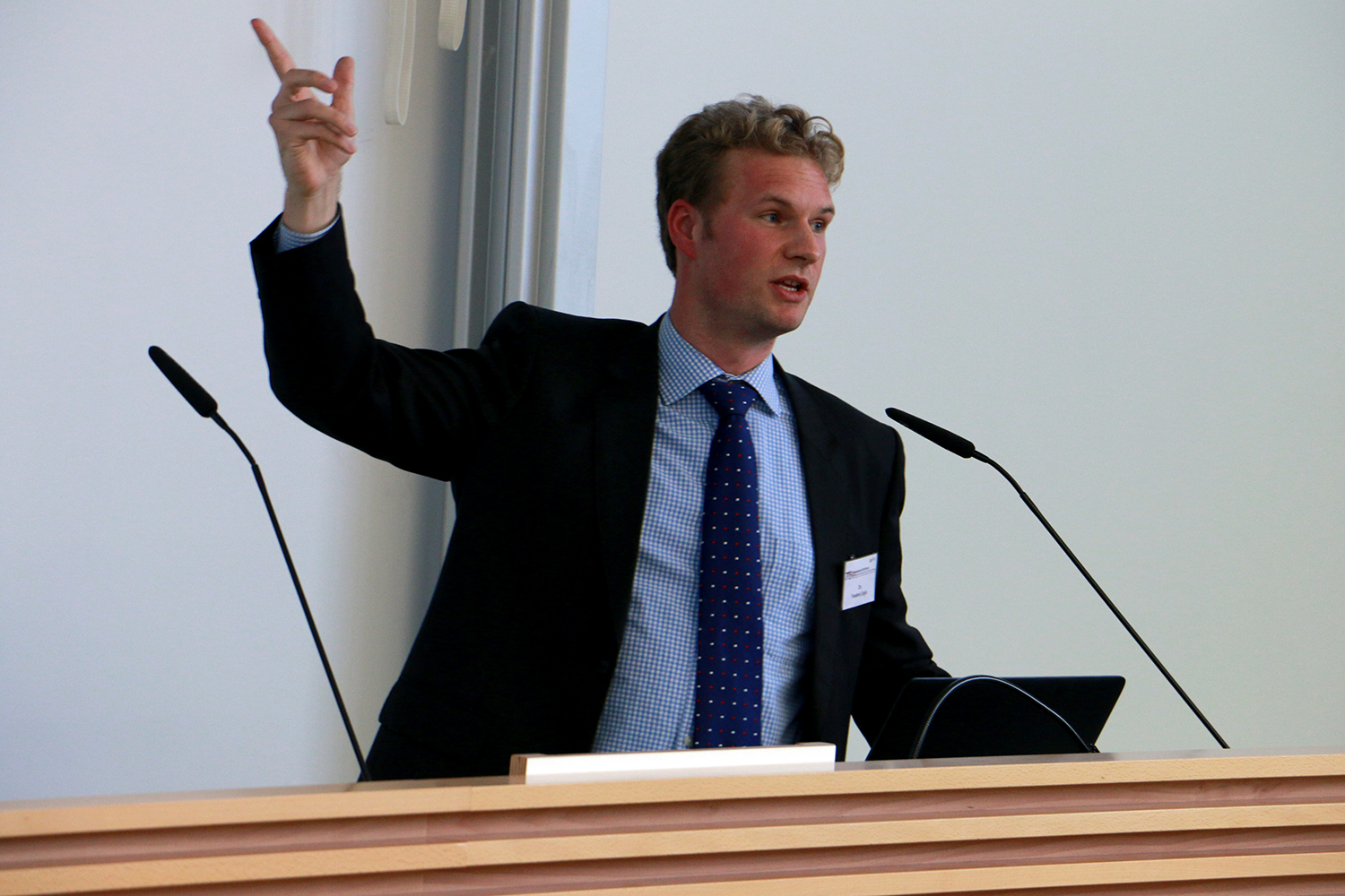 Ein Mann im Anzug gestikuliert nach oben, während er an einem Podium mit zwei Mikrofonen spricht und dabei engagiert wirkt. Der Hintergrund ist zwar neutral, deutet aber auf das prestigeträchtige Ambiente der Hochschule Coburg hin.