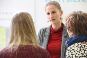 Eine Frau in einem grauen Blazer und einem roten Hemd unterhält sich während der Schnuppertage 2025 mit zwei Frauen, eine mit langen blonden Haaren und eine andere mit kurzen Haaren und einem geblümten Oberteil. Sie scheinen in ein Gespräch in einem gut beleuchteten Innenraum vertieft zu sein. at Hochschule Coburg