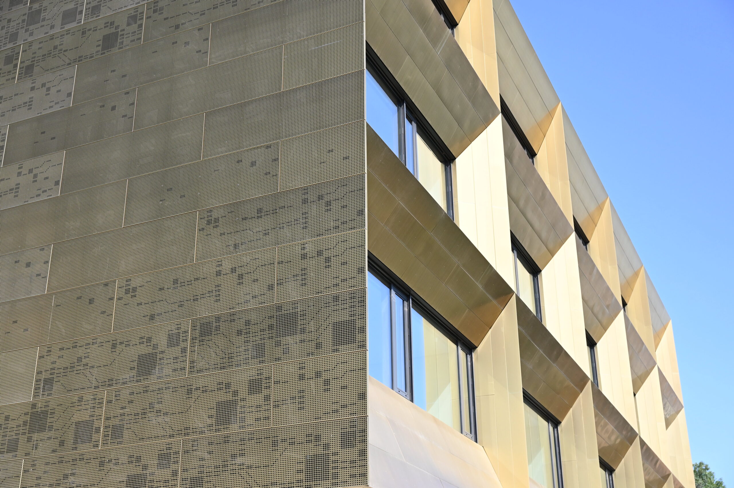 Nahaufnahme der modernen Fassade der Hochschule Coburg. Zu sehen sind links eine gemusterte, strukturierte Wand und rechts große reflektierende Fenster, alles vor einem klaren blauen Himmel.