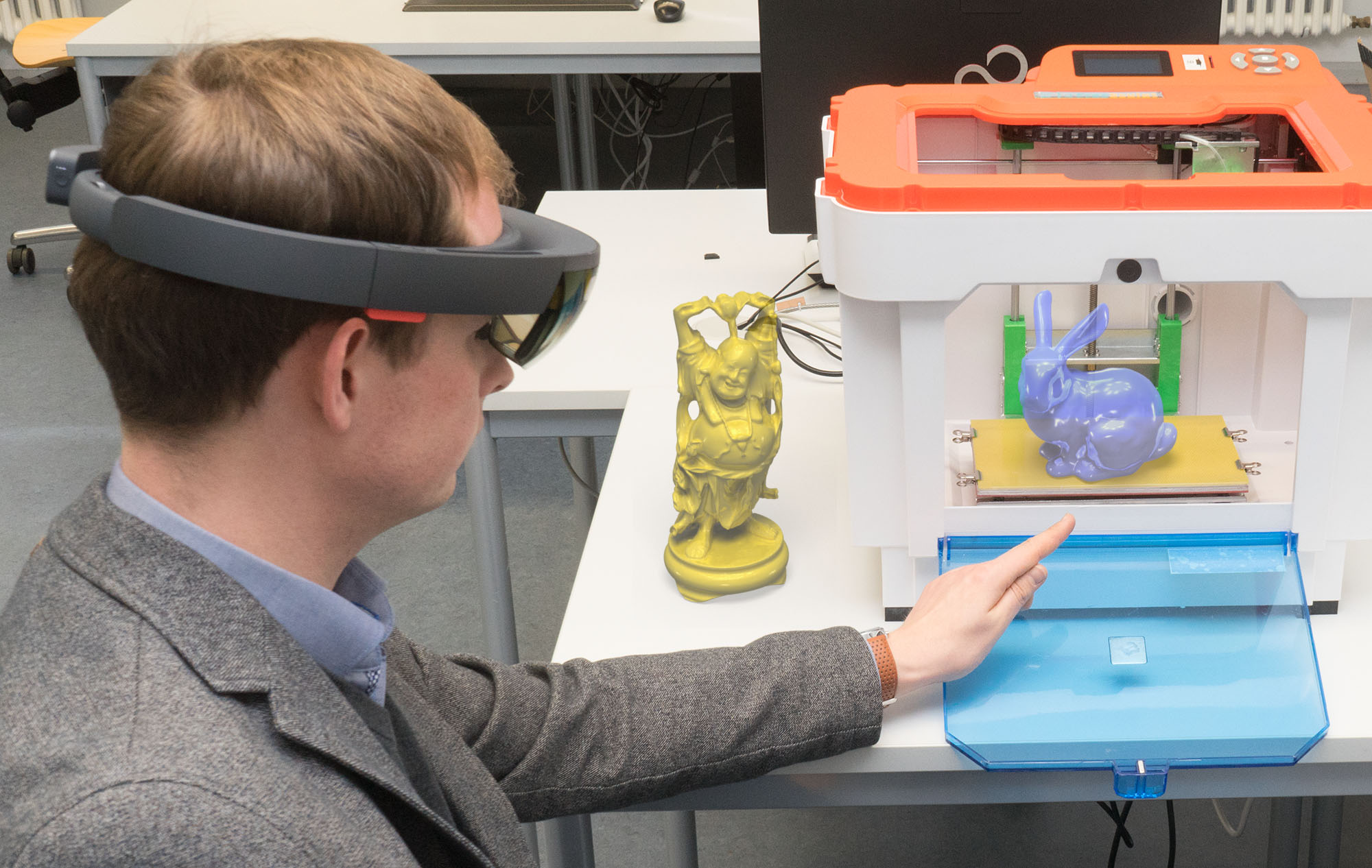 Eine Person mit Augmented-Reality-Brille bedient einen 3D-Drucker an der Hochschule Coburg. Zu sehen sind eine gelbe Statue und ein halbtransparenter blauer 3D-gedruckter Hase, die mit dem Druckergehäuse interagieren.