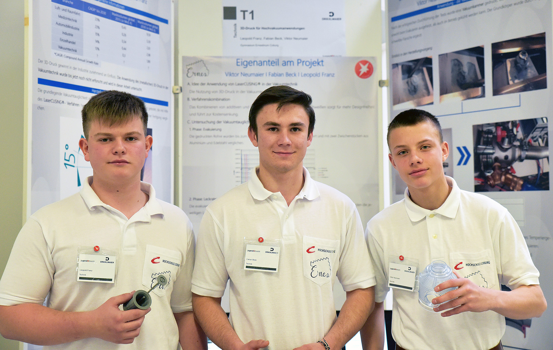 Drei junge Männer in weißen Hemden stehen stolz vor einer Posterpräsentation an der Hochschule Coburg. Sie halten Objekte in den Händen, die mit ihrem Projekt in Zusammenhang stehen, und tragen Namensschilder. Im Hintergrund sind Forschungsmaterial und lebendige Bilder zu sehen, die ihr Engagement und ihre Kreativität widerspiegeln.