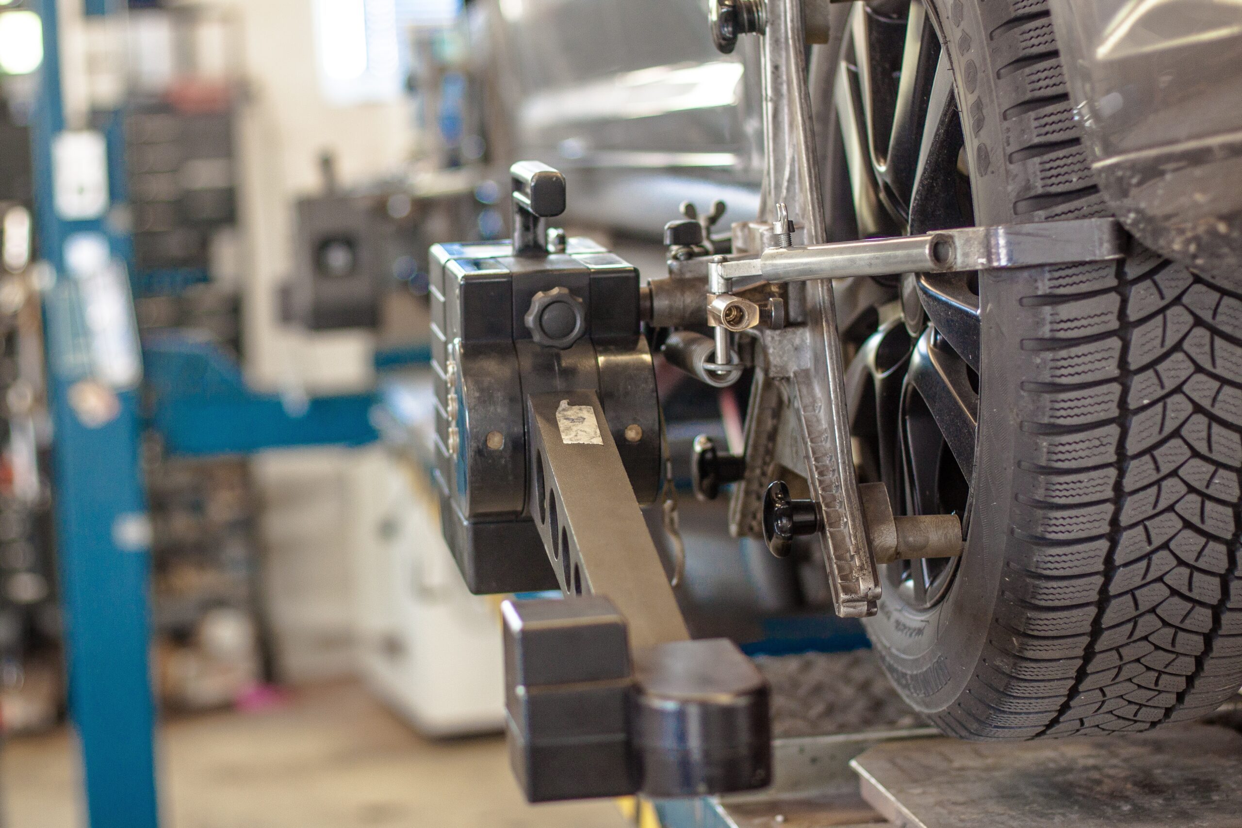 Nahaufnahme eines Autorads auf einer Achsmessmaschine in einer Autowerkstatt. Das an der Felge befestigte Diagnosewerkzeug ist zu sehen. Die Szene spiegelt Präzision wider, die den an der Hochschule Coburg gelehrten Ingenieurstandards entspricht. Ein verschwommener Hintergrund lässt auf die geschäftige Werkstattumgebung schließen.