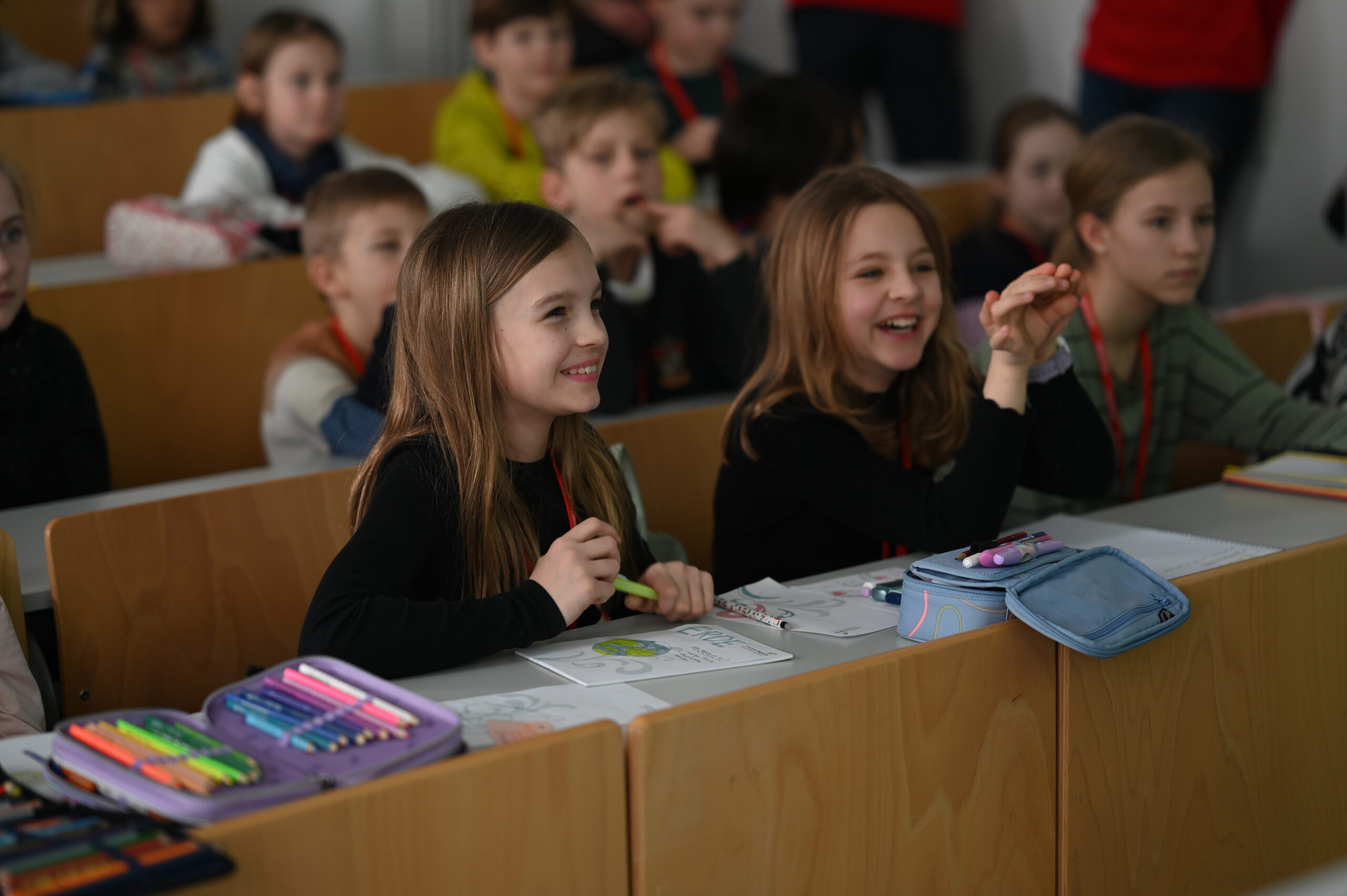 Aufmerksam, lächelnd und engagiert sitzen Kinder im Klassenzimmer der Hochschule Coburg. Ihre bunten Federmäppchen und Blätter sind ordentlich auf ihren Tischen angeordnet. Der Raum summt und summt vor Energie der jungen Schüler, die in mehreren Reihen sitzen und lernbegierig sind.