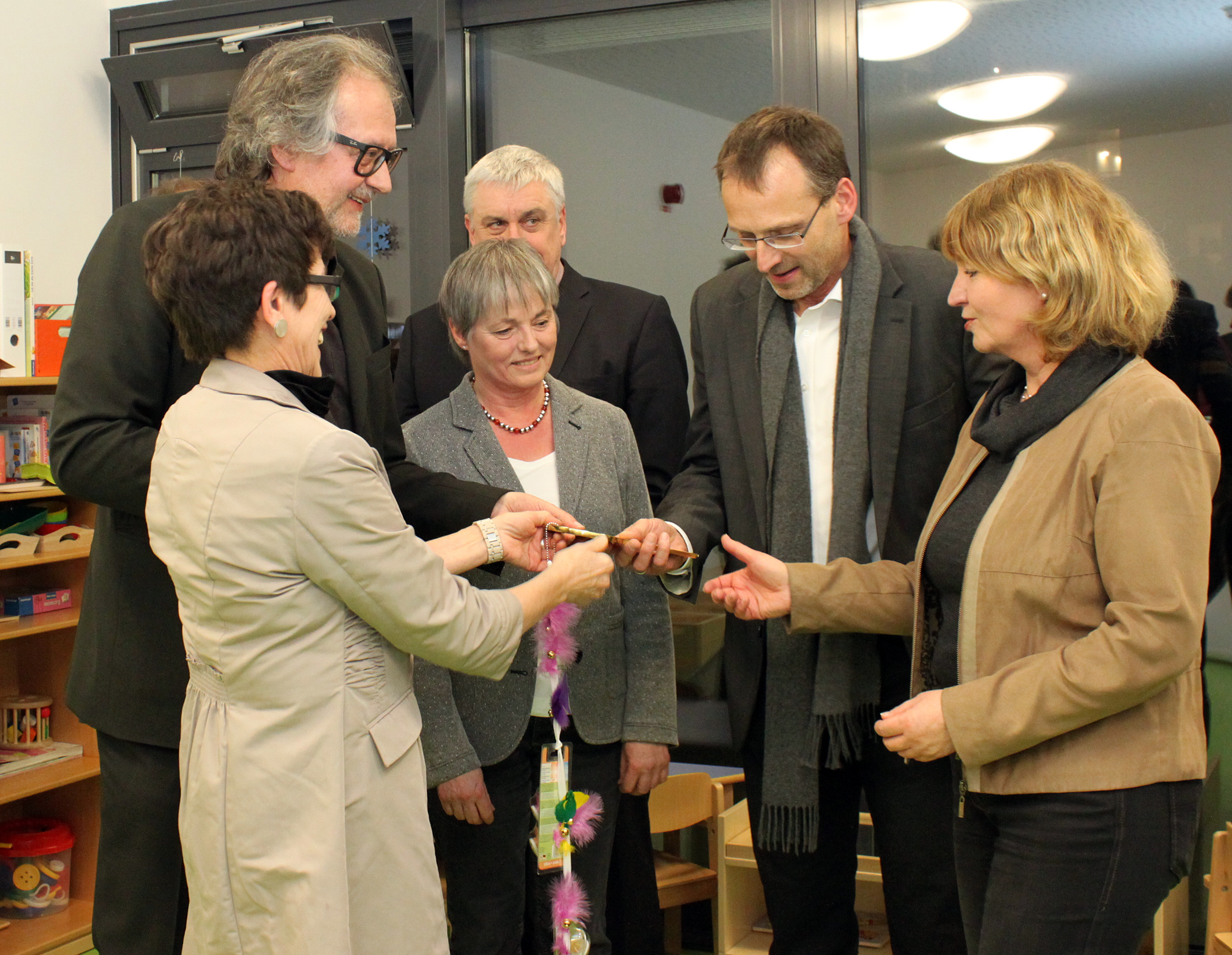 Eine Gruppe von sechs Erwachsenen in Geschäftskleidung versammelt sich im Innenbereich der Hochschule Coburg. Eine Frau überreicht einer anderen, umgeben von Bücherregalen, einen großen dekorativen Schlüssel. Die Atmosphäre ist formell und feierlich, ein bedeutender Anlass an der angesehenen Institution.