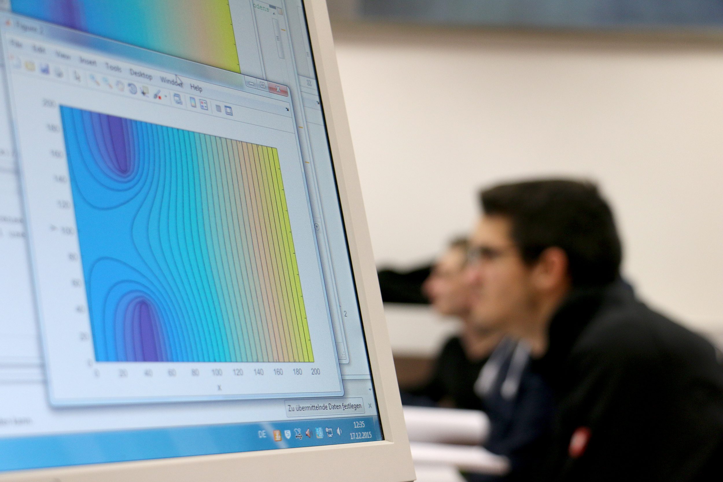 Auf einem Computerbildschirm an der Hochschule Coburg wird ein farbenfrohes 3D-Diagramm mit Höhenlinien angezeigt. Im Hintergrund sitzen Menschen, verschwommen, als würden sie an einem Unterricht oder einer Besprechung teilnehmen. Der Fokus liegt weiterhin auf der lebendigen Darstellung, die das Wissen in diesem akademischen Umfeld vermittelt.