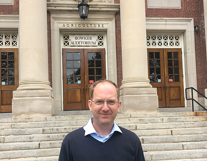 Ein Mann steht vor dem Eingang zum Bowker Auditorium, einem Teil eines Landwirtschaftsgebäudes, das mit seinen großen Säulen und Holztüren an die Hochschule Coburg erinnert.