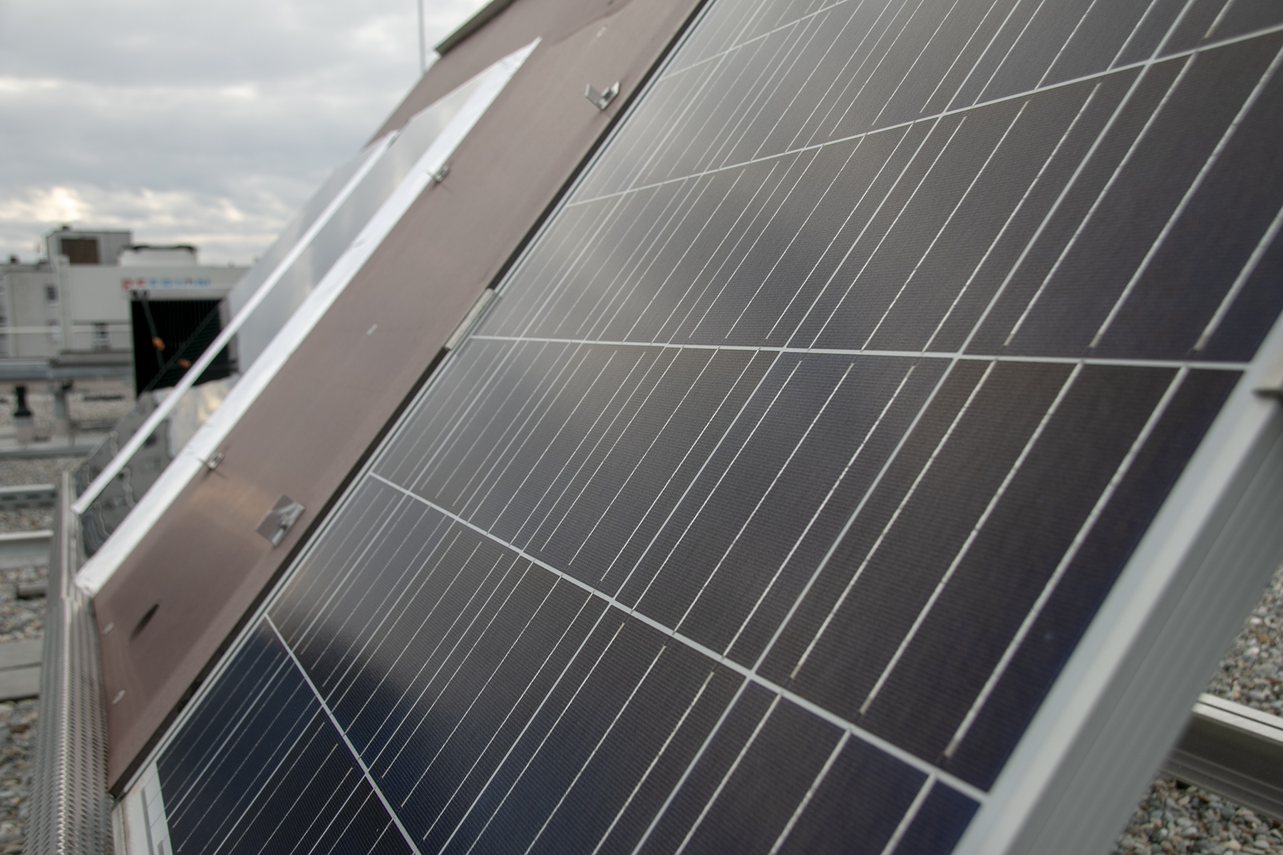 Nahaufnahme von Solarmodulen auf einem Dach der Hochschule Coburg, im Hintergrund ist ein bewölkter Himmel zu sehen. Die Module sind so ausgerichtet, dass sie Sonnenlicht einfangen, und in der Ferne sind verschiedene Gebäude zu sehen.