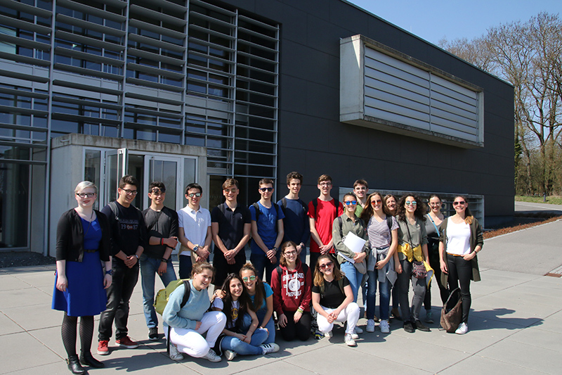 Lächelnd steht eine Gruppe junger Leute vor dem modernen Gebäude der Hochschule Coburg, dessen große Fenster und Lamellen im sonnigen Wetter glänzen. In ihrer legeren Kleidung strahlen sie Kameradschaft und Vorfreude auf den Neuanfang aus.