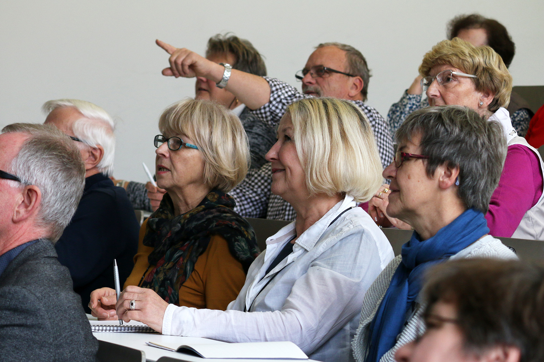 In einer hellen, akademischen Atmosphäre an der Hochschule Coburg sitzt eine Gruppe älterer Erwachsener aufmerksam in einem Klassenzimmer. Eine Person zeigt nach vorne, während sie sich auf die Vorlesung konzentrieren. Notizbücher und Stifte liegen bereit, um jedes aufschlussreiche Detail festzuhalten.