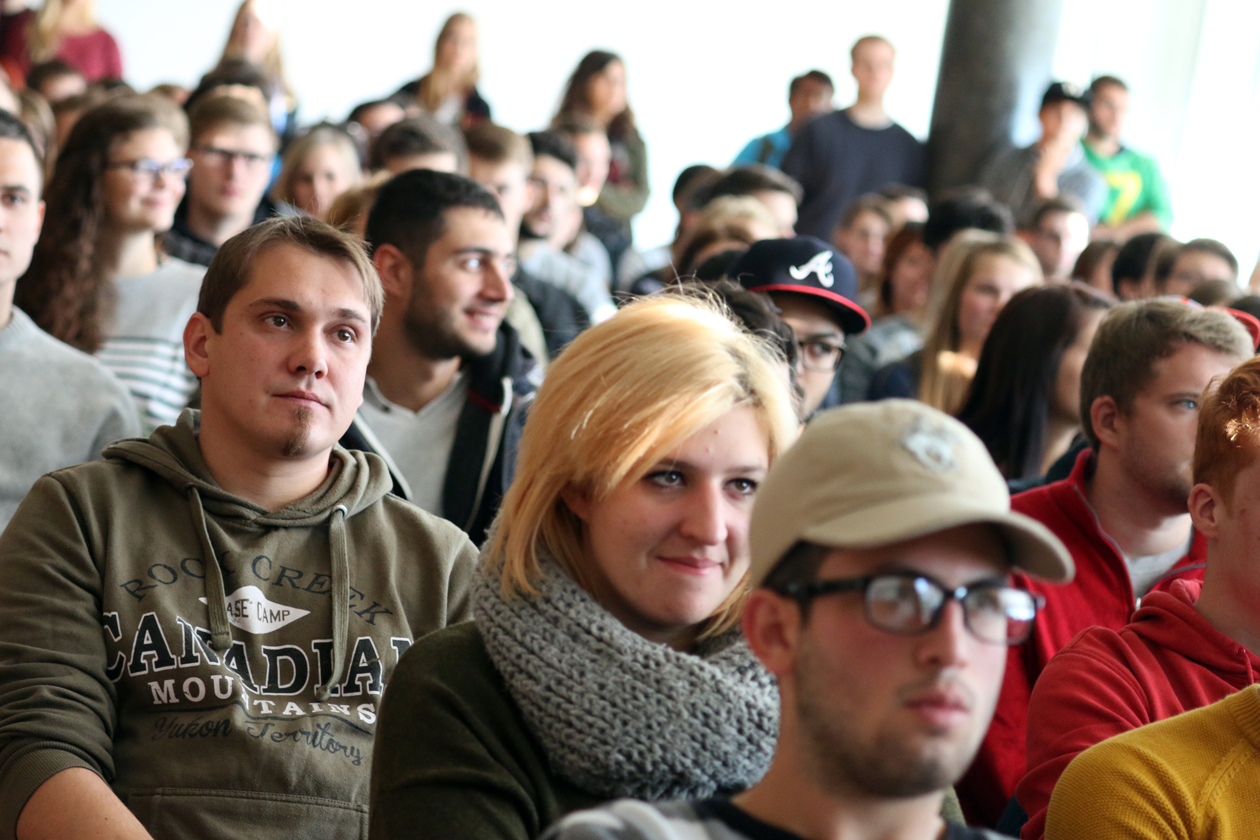 Eine bunt gemischte Gruppe sitzt in einem überfüllten Raum der Hochschule Coburg und hört einem Vortragenden aufmerksam zu. Im Publikum sind Menschen unterschiedlichen Alters, manche tragen Brillen, andere sind leger gekleidet. Die Atmosphäre wirkt engagiert und konzentriert.