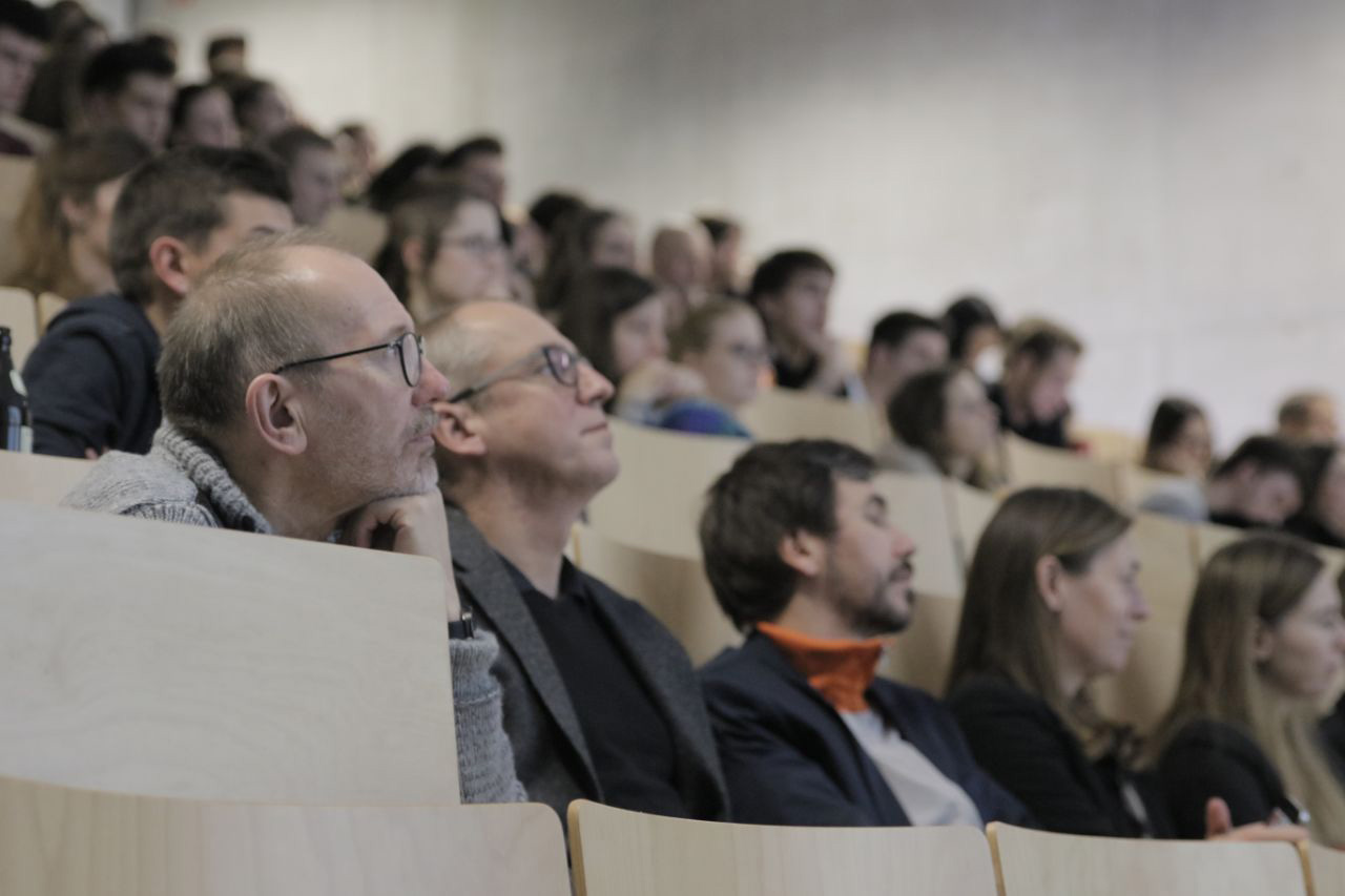 In einem Hörsaal der Hochschule Coburg sitzt eine Gruppe aufmerksamer Personen in Sitzreihen und konzentriert sich auf die Präsentation. Im Raum herrscht reges Treiben, denn sowohl Männer als auch Frauen vertiefen sich in die Vorlesung.