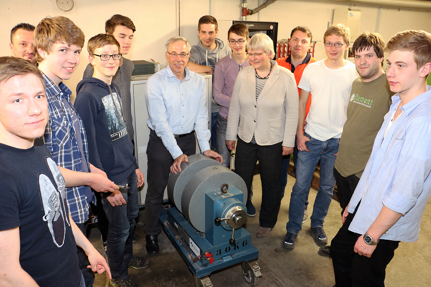 Eine Gruppe von Menschen, darunter Studenten und Erwachsene der Hochschule Coburg, steht in einer Werkstatt oder einem Labor um eine große Maschine mit der Aufschrift „30 KG“. Sie blicken alle in die Kamera und lächeln.