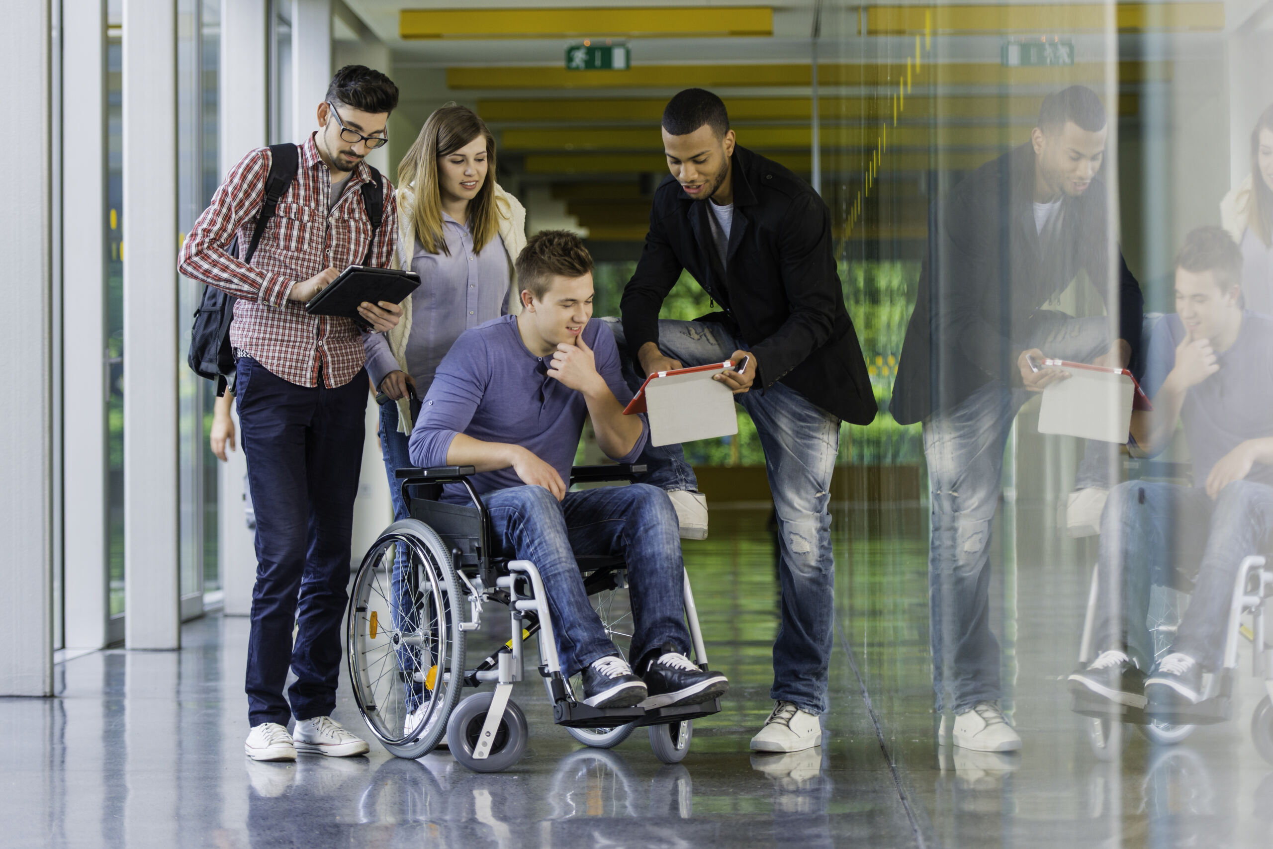 Group of young students using digital tablets and mobile phones in the corridor of the college.