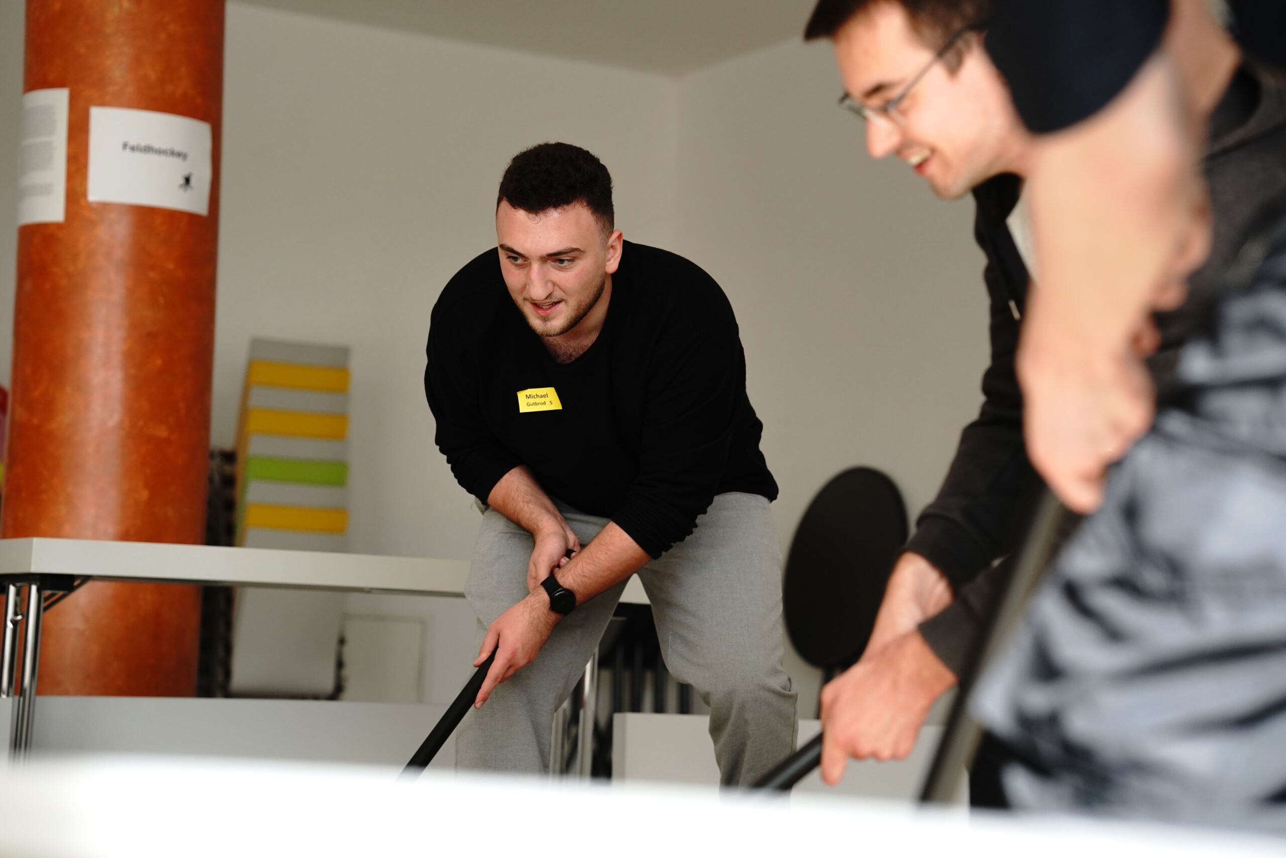 Studis spielen Feldhockey in einem Gebäude