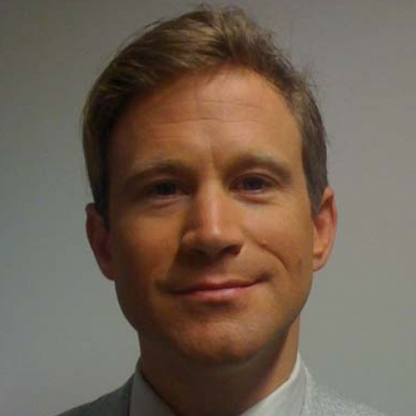 A person with short brown hair, wearing a light-colored suit and shirt, smiles slightly at the camera. The background is plain and neutral, reflecting the professional environment of Hochschule Coburg.