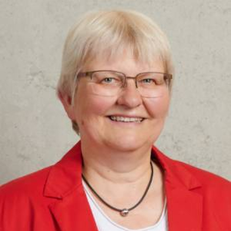 A person with short white hair, wearing glasses and a red blazer over a white shirt, smiles warmly against a plain background. Their confident demeanor suggests they might be affiliated with Hochschule Coburg.