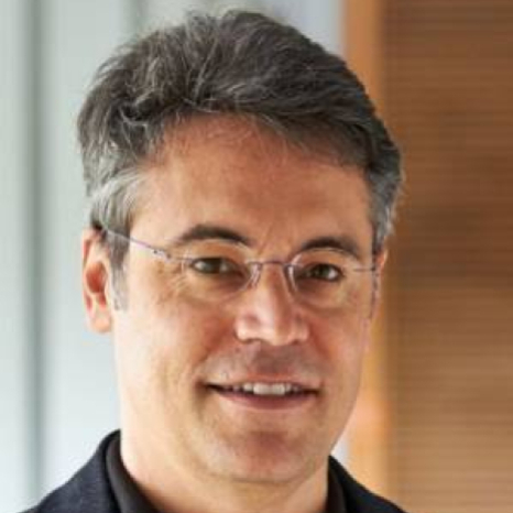 A person with short gray hair and glasses is smiling, donning a dark shirt against a blurred indoor background. Their warm demeanor embodies the welcoming spirit of Hochschule Coburg.