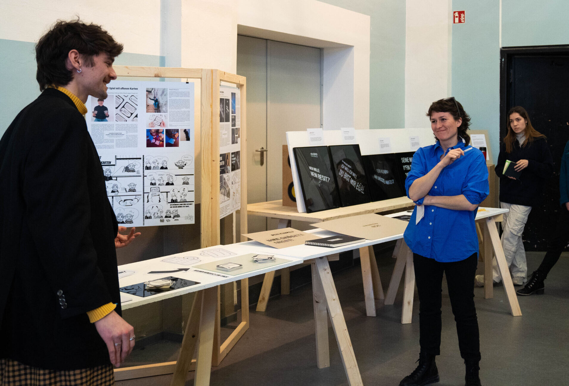 Eine Gruppe von Menschen beobachtet in einer Galerie einen Mann, der seine Arbeit präsentiert. In der ungezwungenen Atmosphäre wird über dieses Studierenden-Projekt diskutiert, in dem Architekturzeichnungen und Fotografien gezeigt werden, die Design-Aktivismus mit kreativer Vision verbinden. at Hochschule Coburg