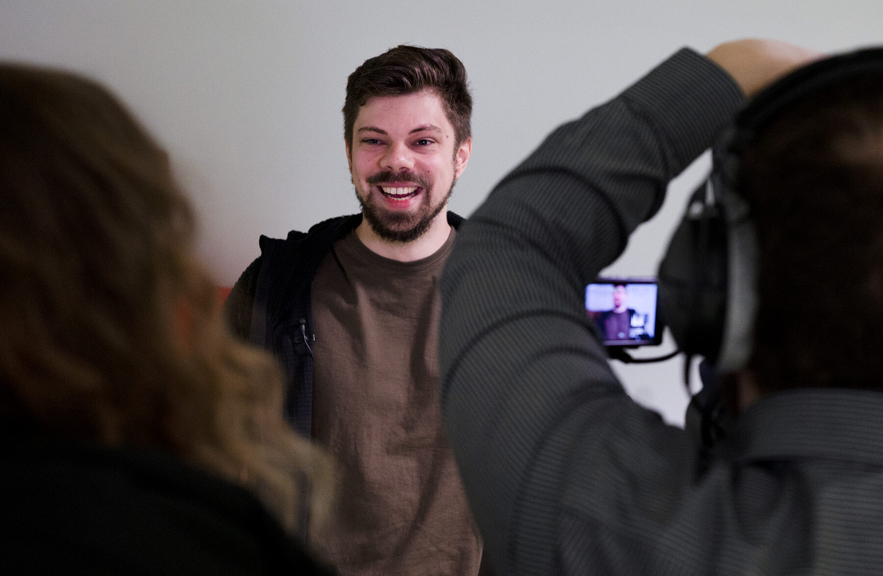 Ein Mann mit Bart lächelt in die Kamera und strahlt Selbstbewusstsein aus. Er trägt ein braunes Hemd und eine schwarze Jacke. at Hochschule Coburg