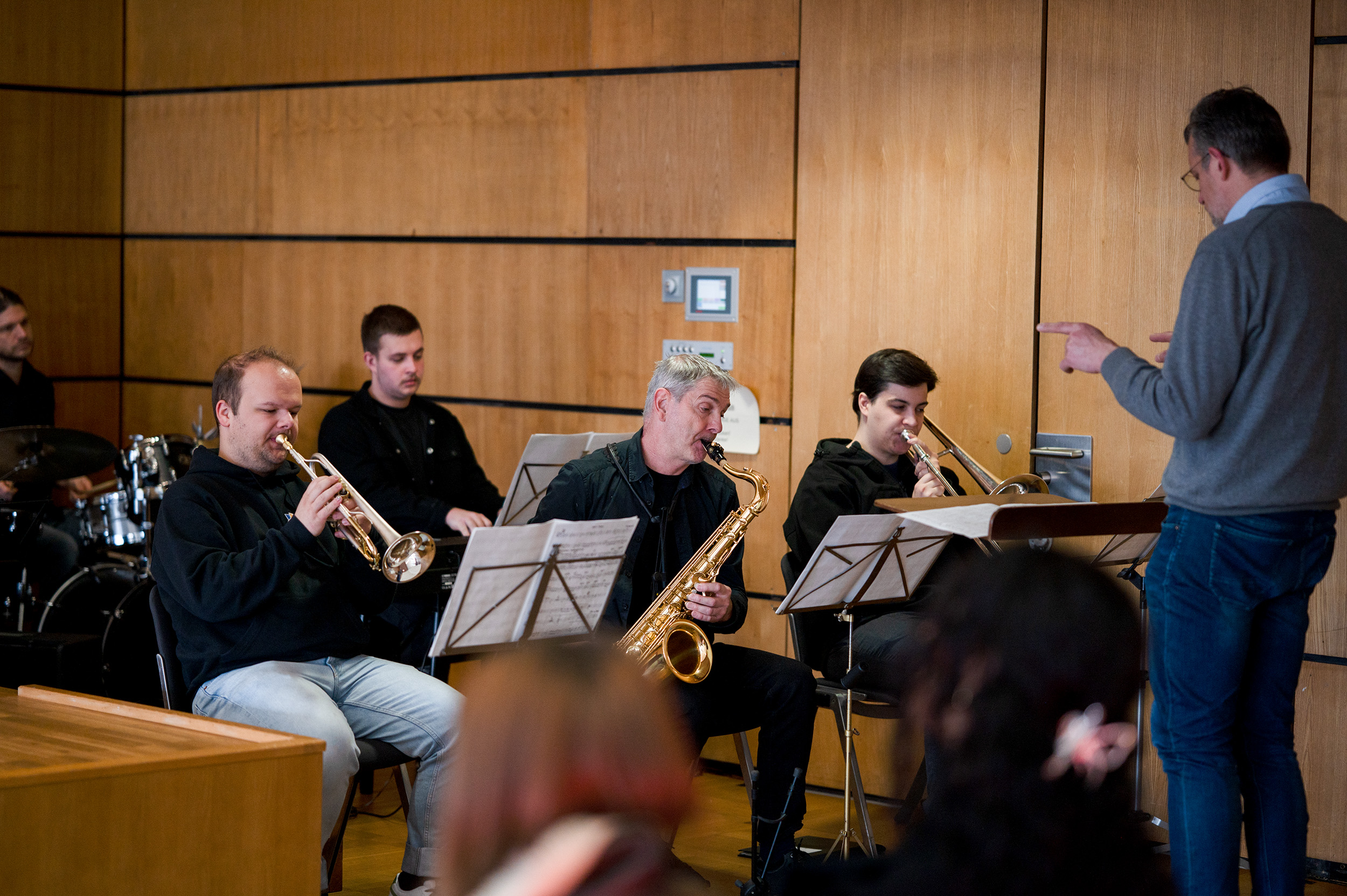 Zu Semesterbeginn probt ein Musikensemble im Gebäude. Vier Musiker mit Trompeten und Saxophonen lesen Noten, während ein Dirigent nach vorne gestikuliert. Im Hintergrund des holzgetäfelten Raumes ist ein Schlagzeuger zu sehen, der eine harmonische Mischung schafft, die an die Verwaltung internationaler Finanzen erinnert. at Hochschule Coburg