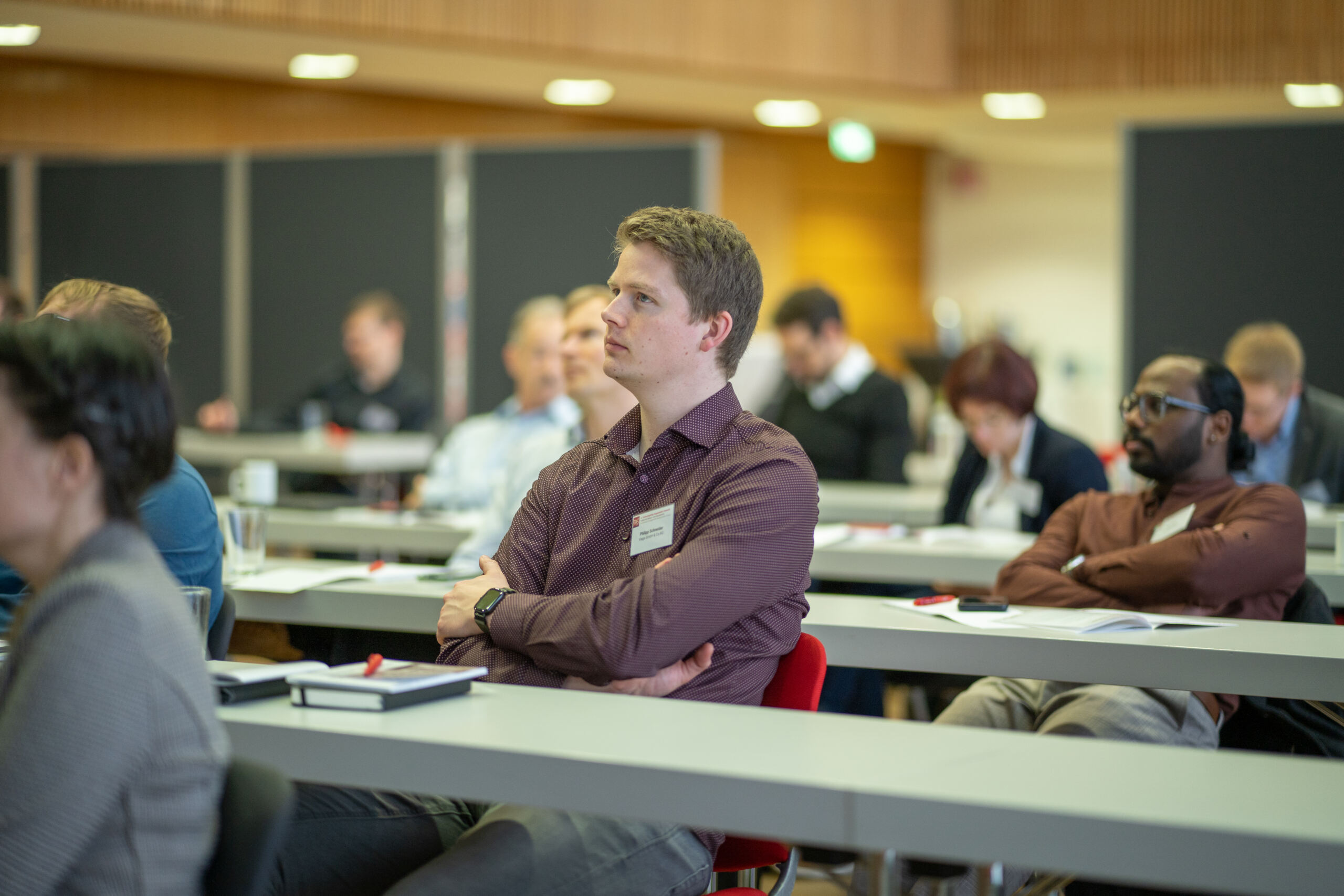 Menschen sitzen in einem Konferenzraum und hören aufmerksam zu. Sie sitzen an langen Tischen, vor ihnen liegen Notizbücher und Stifte. Der moderne Raum, der für Medizintechnik-Konferenzen konzipiert wurde, verfügt über eine helle Beleuchtung, die die konzentrierte Atmosphäre verstärkt. at Hochschule Coburg